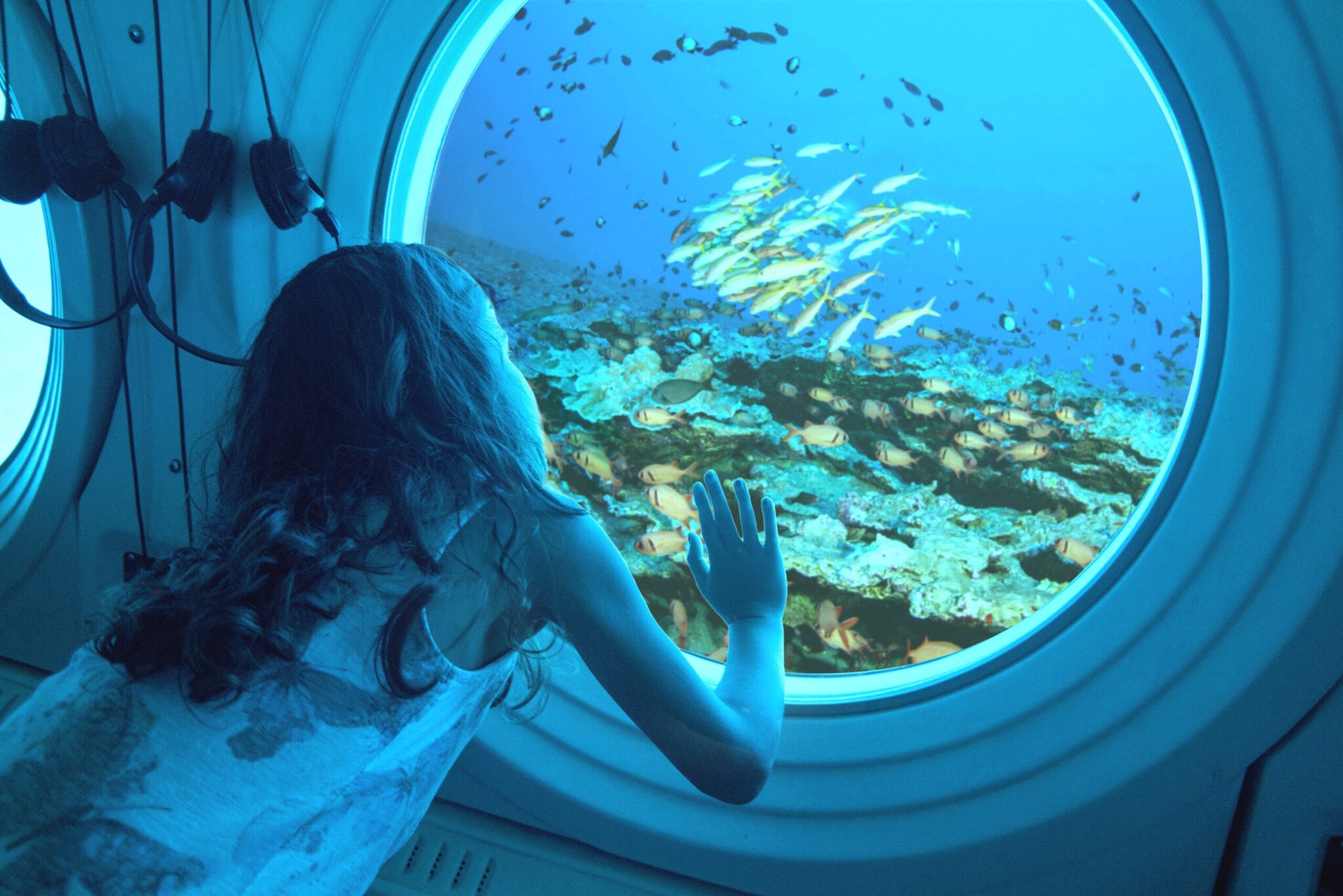 Ein Mädchen schaut durch ein Bullauge in einem U-Boot auf Fische und Korallen. Ein Mädchen schaut durch ein Bullauge in einem U-Boot auf Fische und Korallen.
