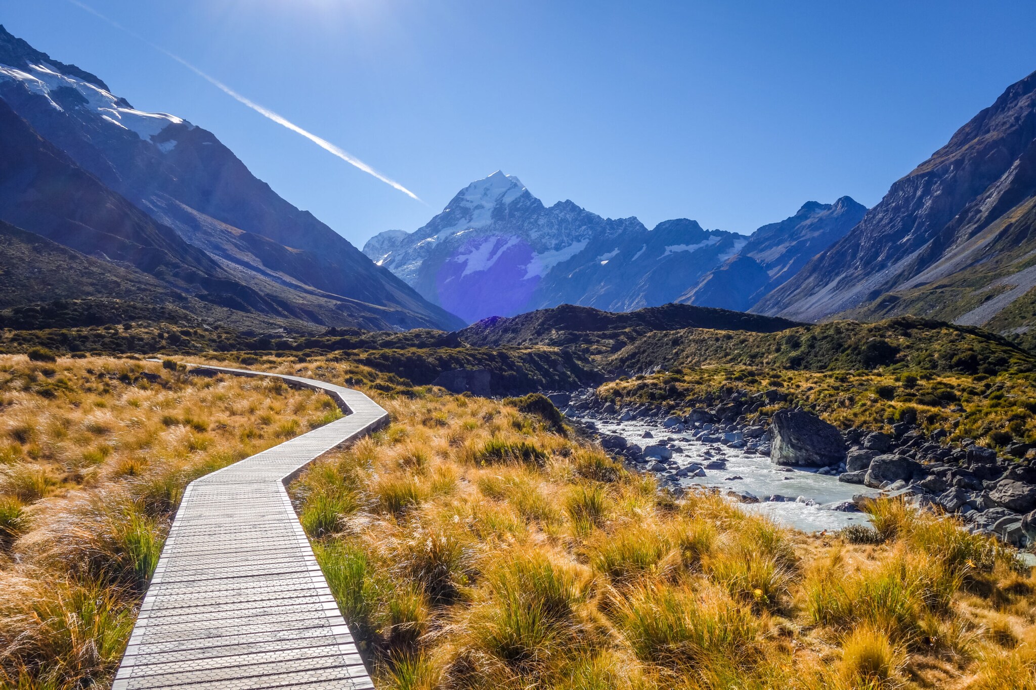 Wilde Landschaft des Mount-Cook-Nationalparks mit Bergpanorama, durch die ein Holzsteg führt Wilde Landschaft des Mount-Cook-Nationalparks mit Bergpanorama, durch die ein Holzsteg führt