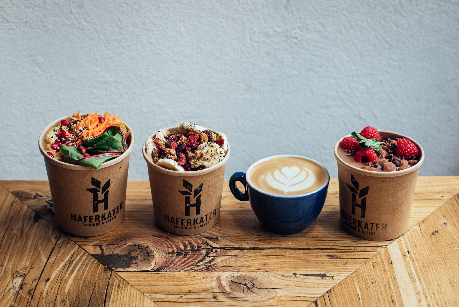 Drei mit Porridge und Obst gefüllte Becher und ein Cappuccino. Drei mit Porridge und Obst gefüllte Becher und ein Cappuccino.