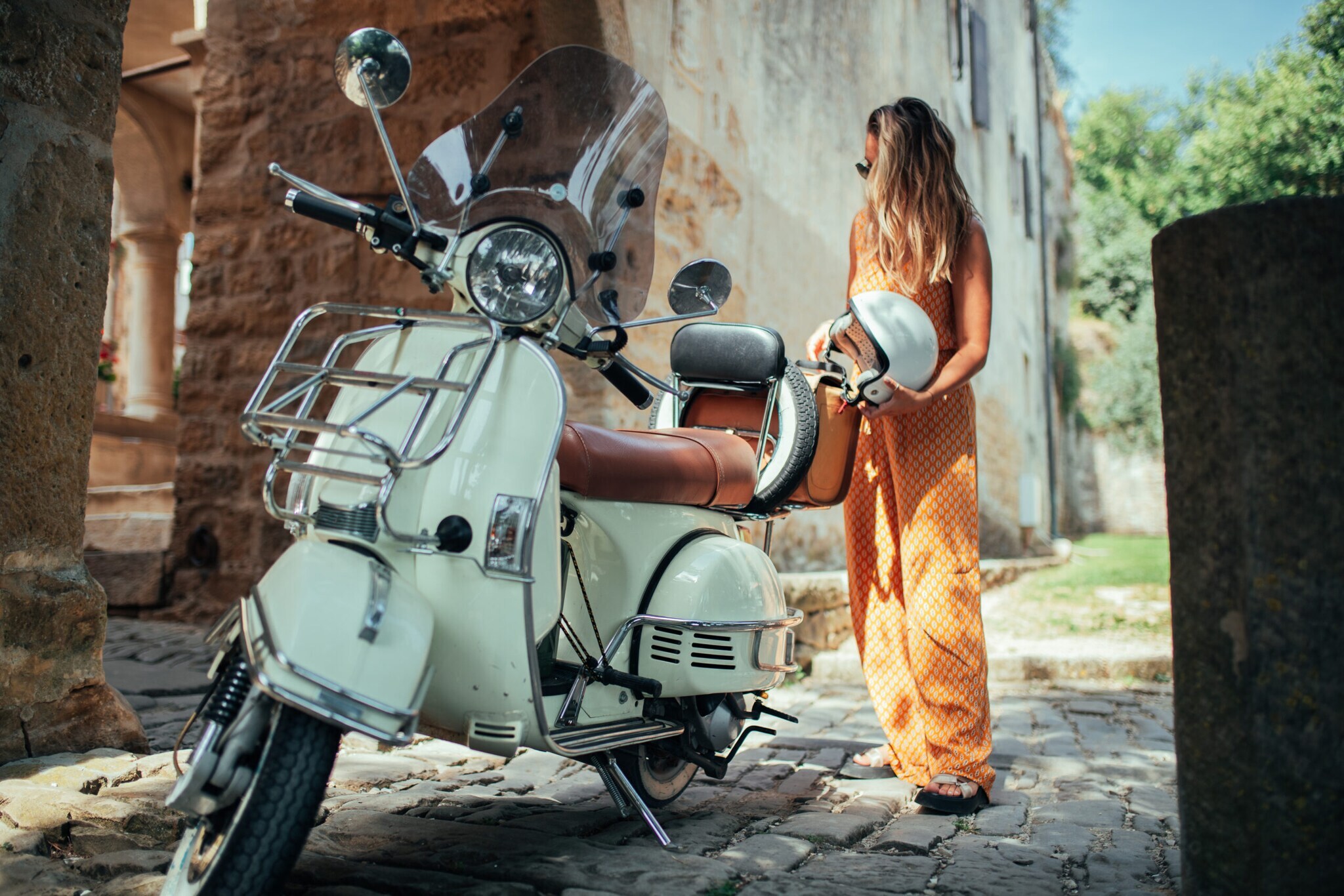 Depicting a beautiful woman on a vespa, cruising through old city town.