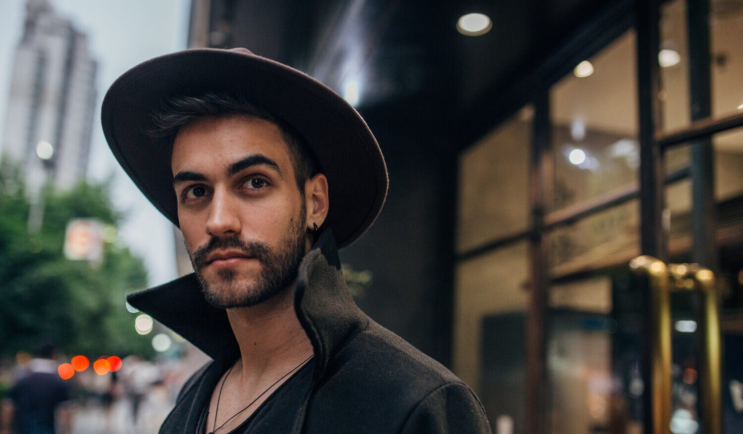 Porträtaufnahme eines jungen, stylishen Mannes mit Hut in urbaner Umgebung