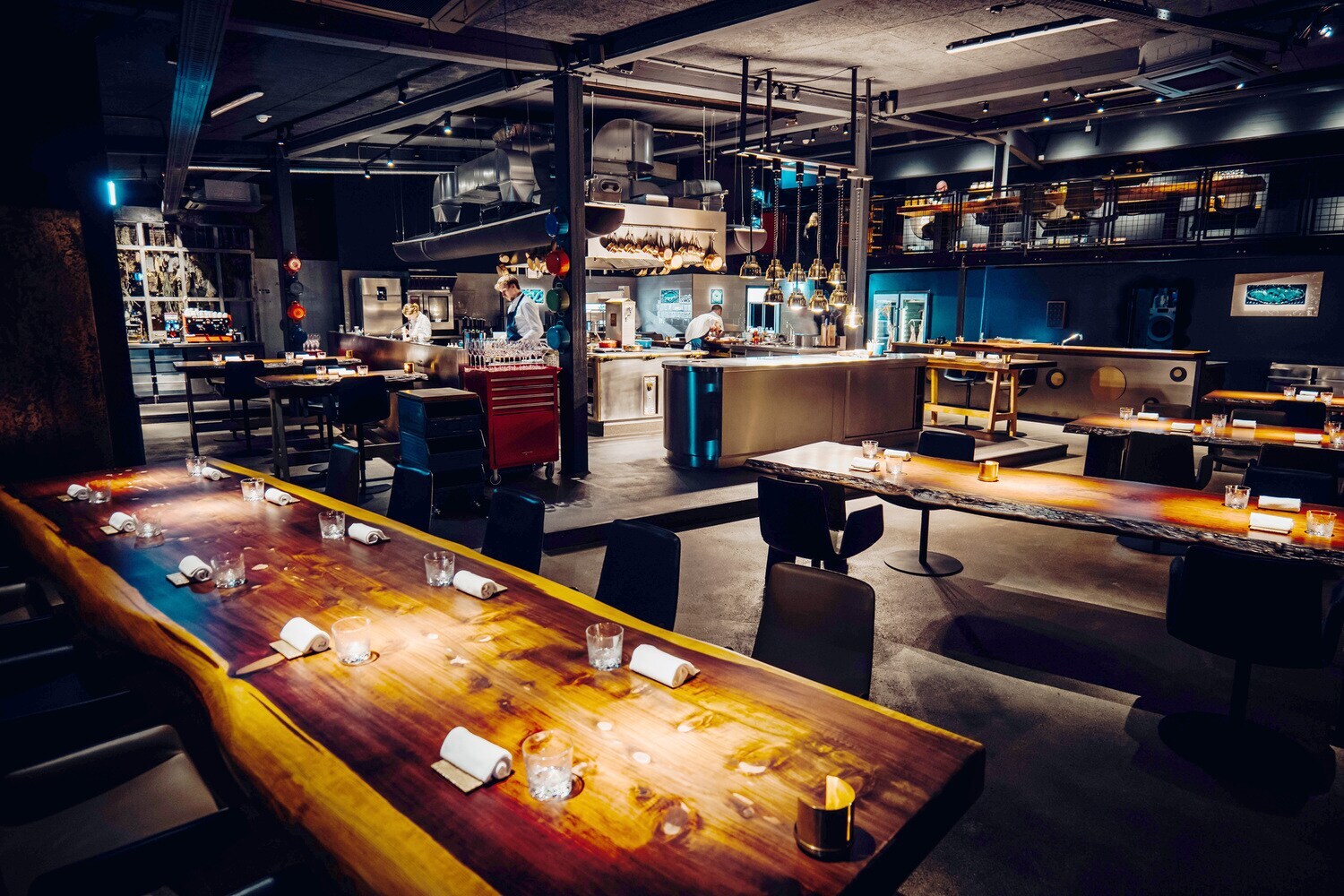 Blick in ein Restaurant mit Holztischen und mittiger Kücheninsel