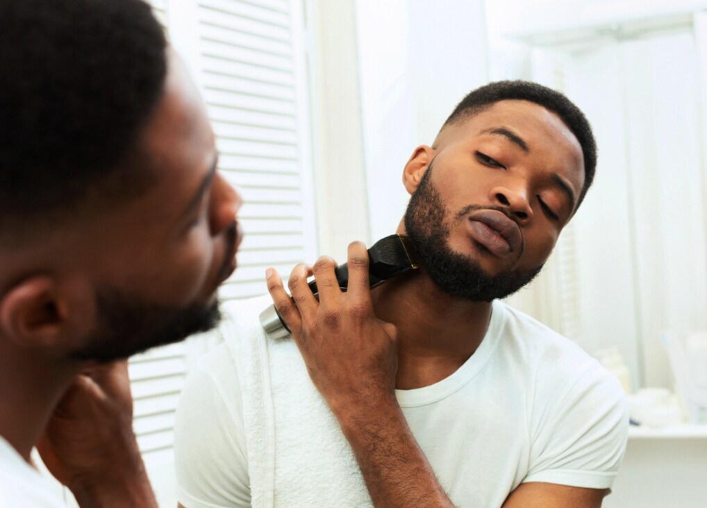 Ein Mann steht vor einem Spiegel und trimmt mit einem Barttrimmer seinen Bart