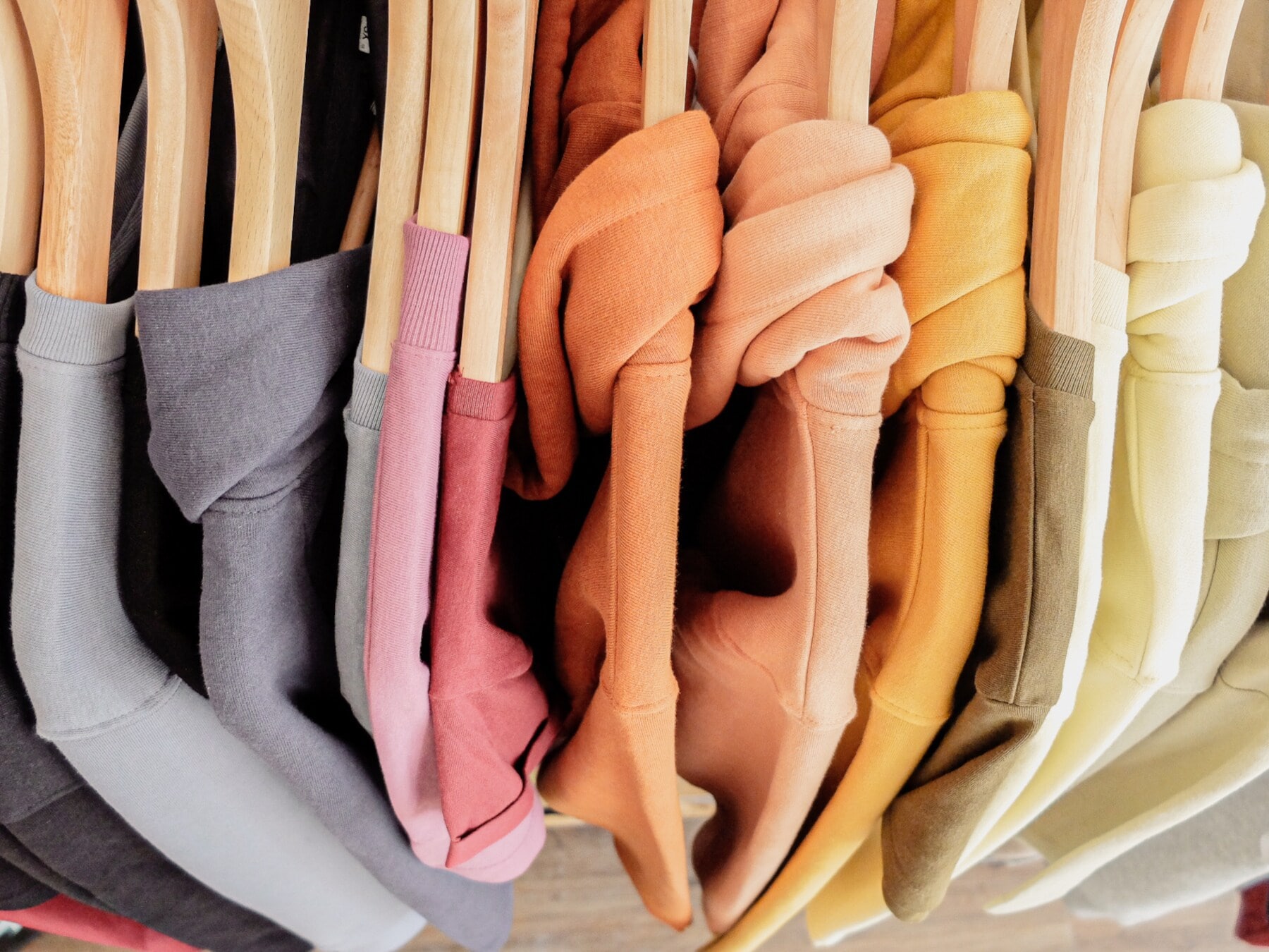 Eine Reihe Sweatshirts in bunten Pastellfarben auf Kleiderbügeln aus Holz Eine Reihe Sweatshirts in bunten Pastellfarben auf Kleiderbügeln aus Holz