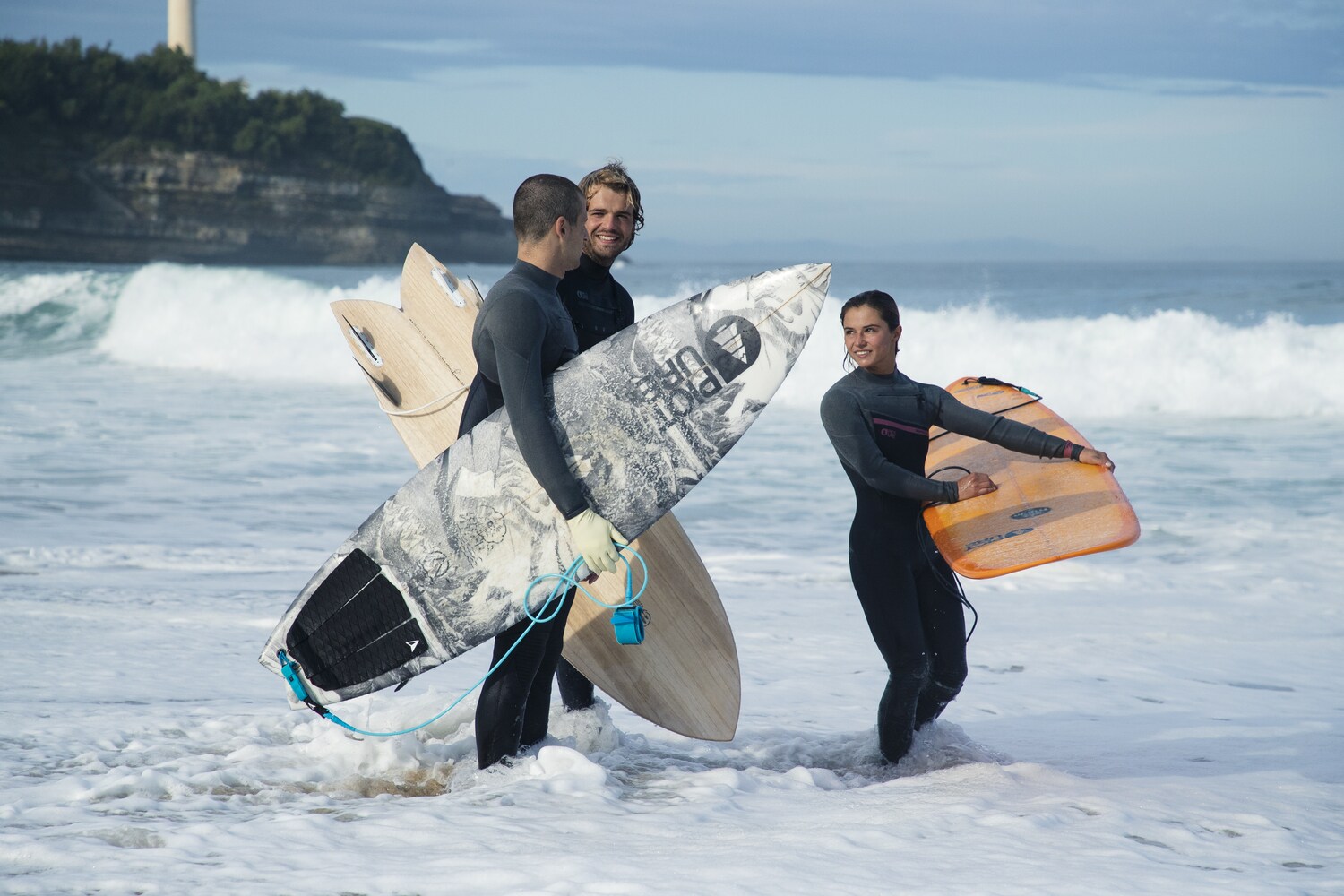 Drei Menschen stehen in Neoprenkleidung und Surfbrettern im Wasser. Drei Menschen stehen in Neoprenkleidung und Surfbrettern im Wasser.