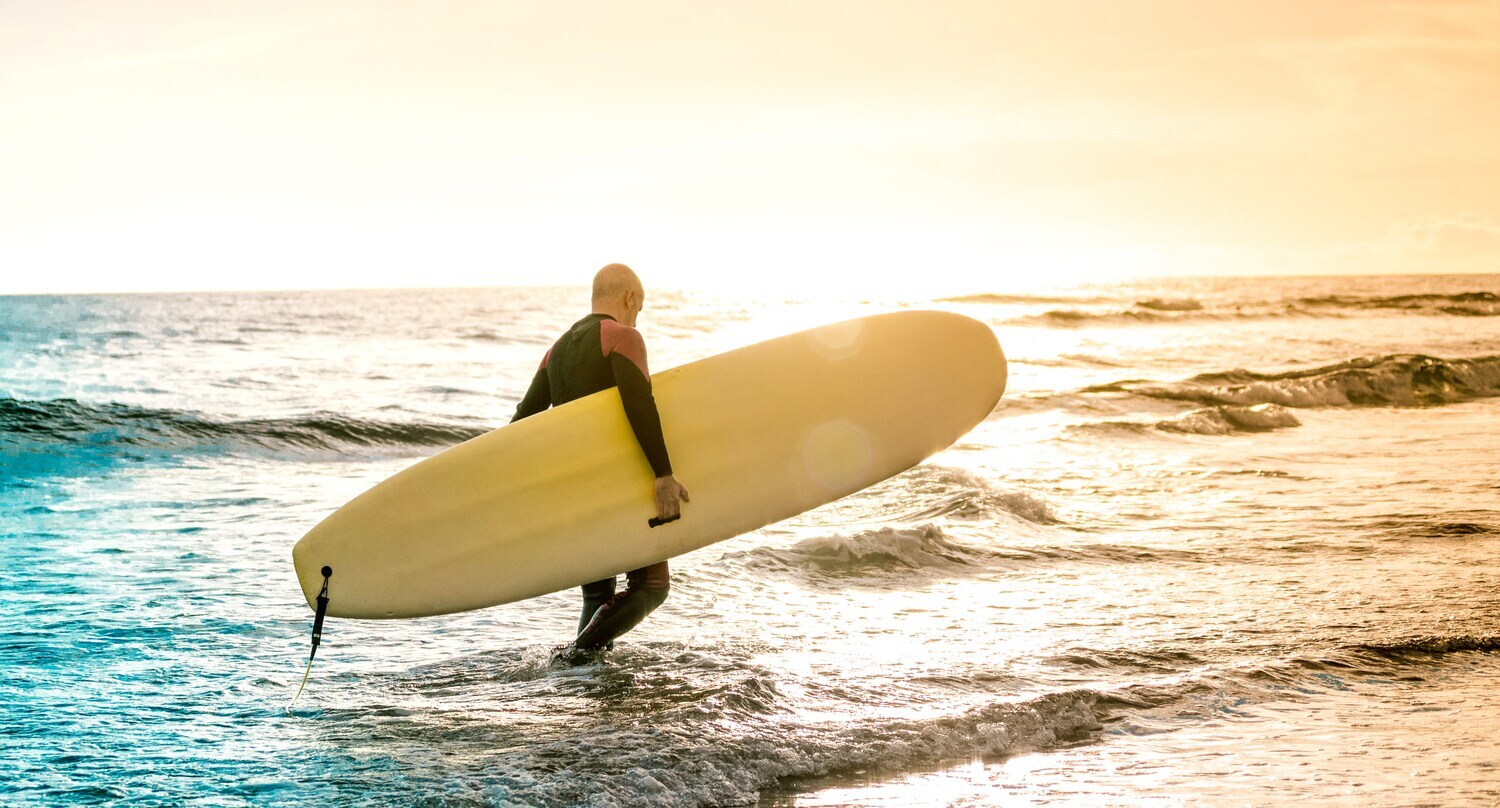 Ein Surfer trägt sein Surfboard durch das Wasser im Sonnenuntergangslicht. Ein Surfer trägt sein Surfboard durch das Wasser im Sonnenuntergangslicht.