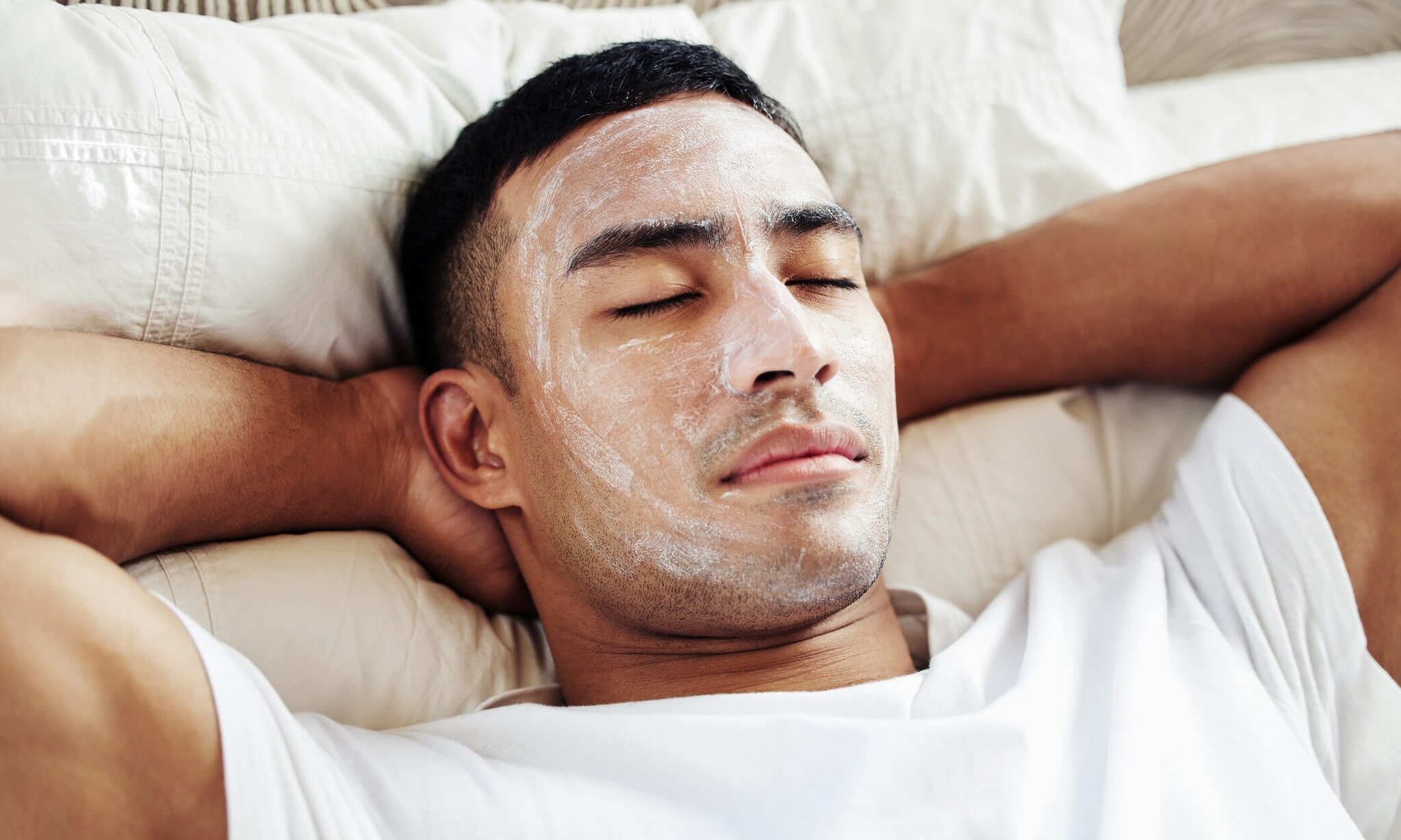 Ein Mann, der eine kosmetische Gesichtsmaske trägt, während er zu Hause auf seinem Bett liegt Ein Mann, der eine kosmetische Gesichtsmaske trägt, während er zu Hause auf seinem Bett liegt