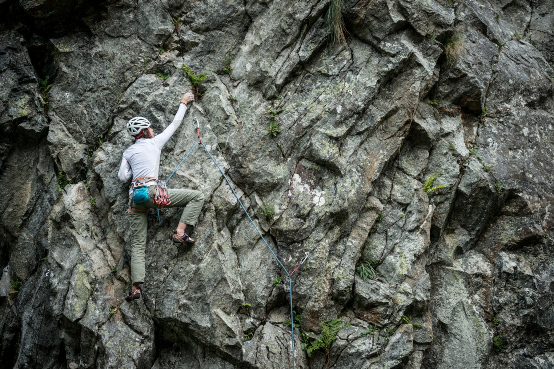 Eine junge Frau mit Helm klettert mit einem Seil an einer Felswand empor