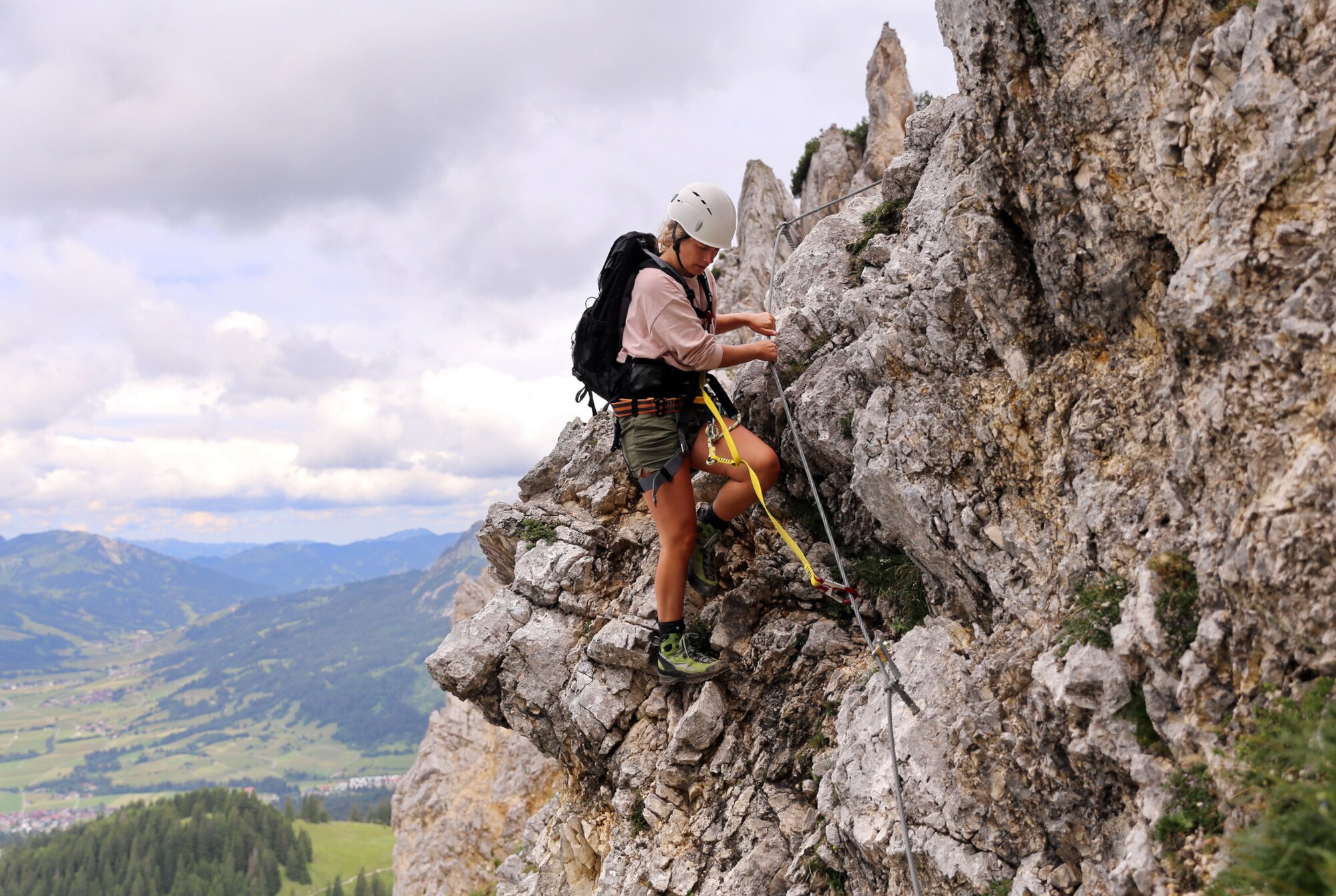 Eine junge Frau klettert am Friedberger Klettersteig am Seil entlang