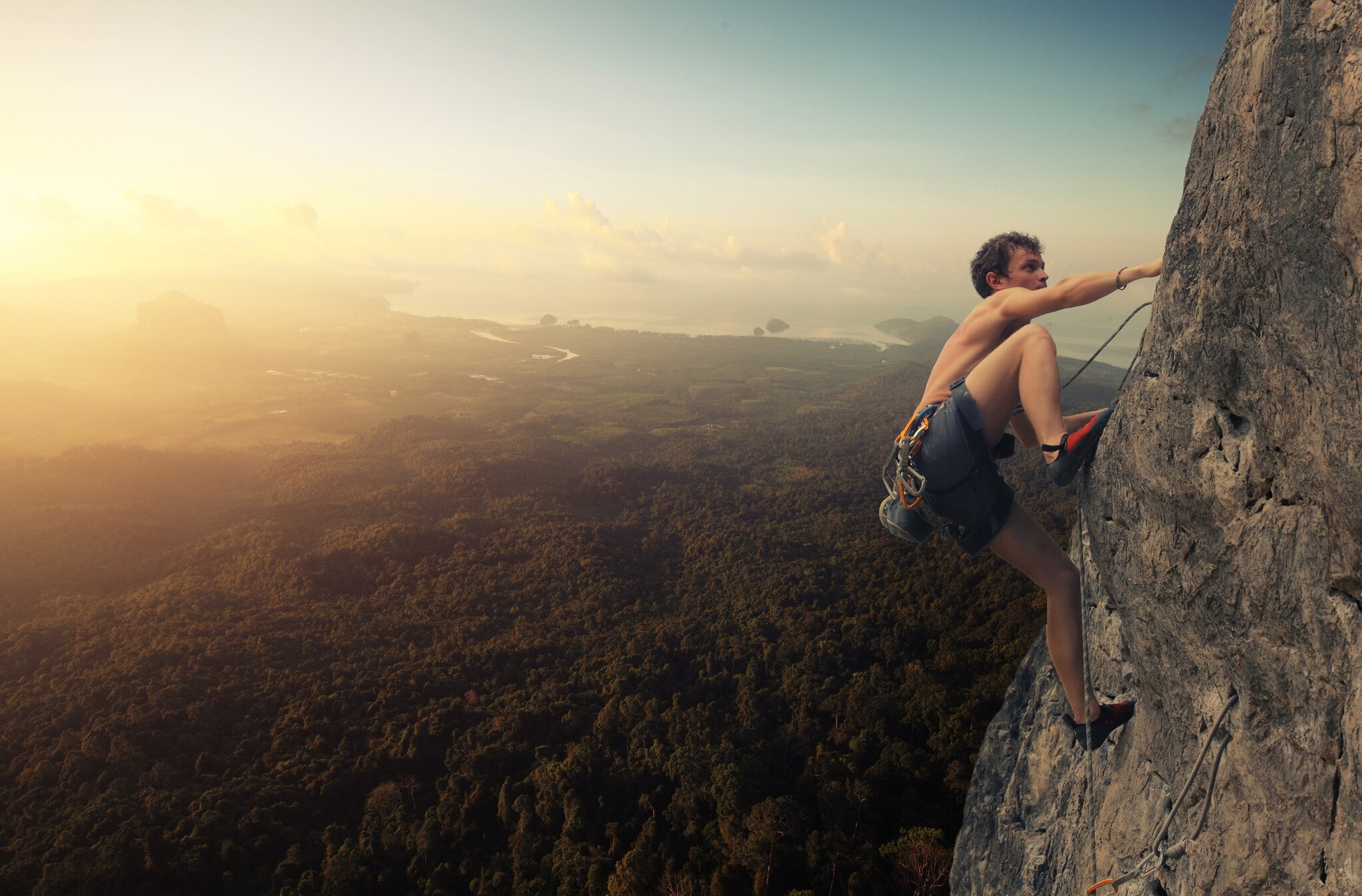Ein junger Mann klettert an einer Felswand, während die Sonne untergeht Ein junger Mann klettert an einer Felswand, während die Sonne untergeht