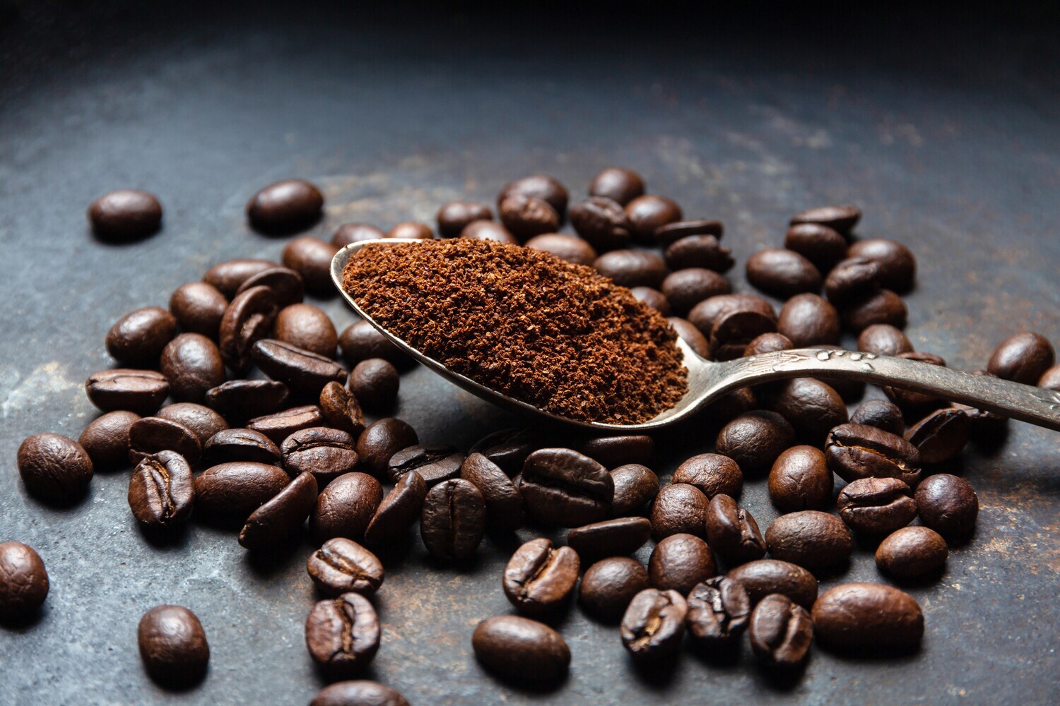 Ein Löffel mit Kaffeepulver liegt auf mehreren Kaffeebohnen.
