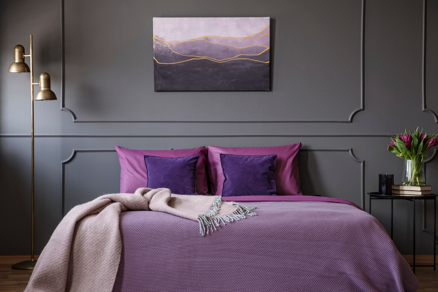 Ein elegantes Schlafzimmer mit einem Doppelbett mit Kissen und Decke in Violetttönen vor einer grauen Wand Ein elegantes Schlafzimmer mit einem Doppelbett mit Kissen und Decke in Violetttönen vor einer grauen Wand