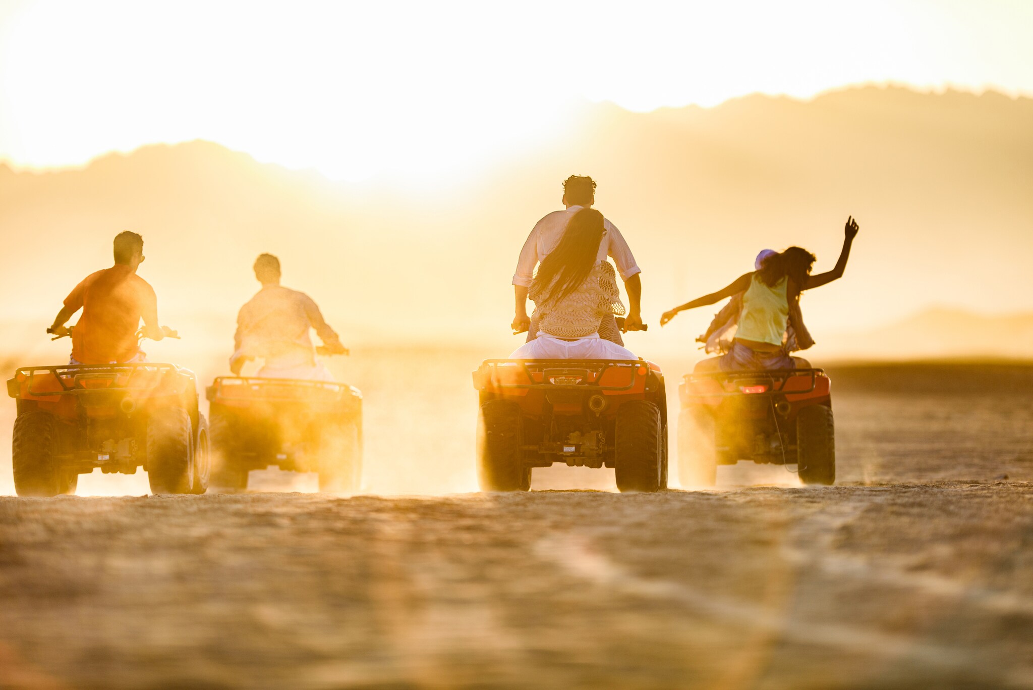 Eine Gruppe Menschen fährt auf Quads über den Sand bei Sonnenuntergang Eine Gruppe Menschen fährt auf Quads über den Sand bei Sonnenuntergang