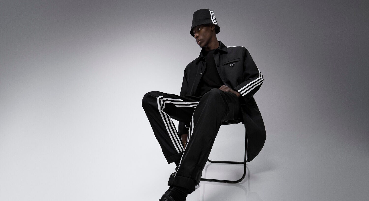 Ein männliches Model mit schwarzem Trainingsanzug von adidas sitzt auf einem Stuhl. Ein männliches Model mit schwarzem Trainingsanzug von adidas sitzt auf einem Stuhl.