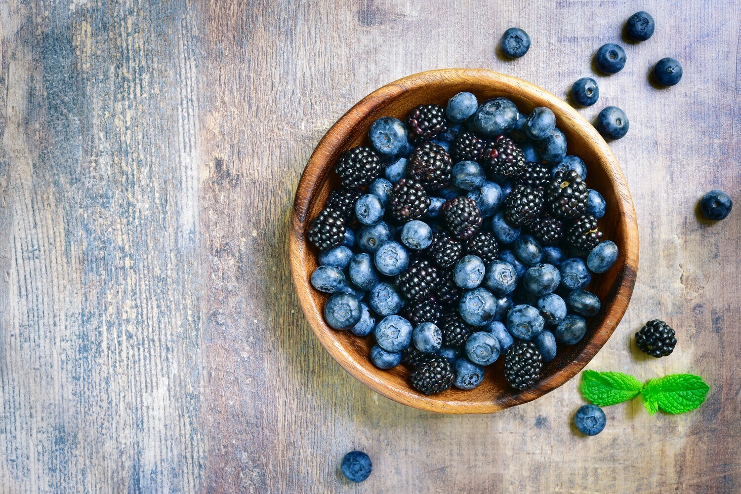Heidelbeeren und Brombeeren in einer Holzschale.