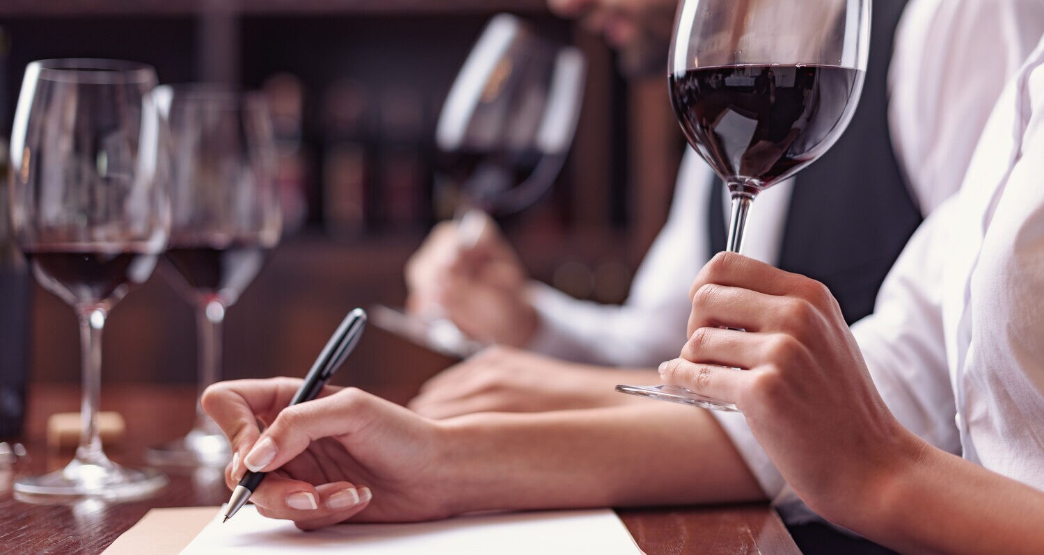 Zwei Menschen halten ihre Nase dicht über einem Rotweinglas und schnüffeln an dem Getränk.