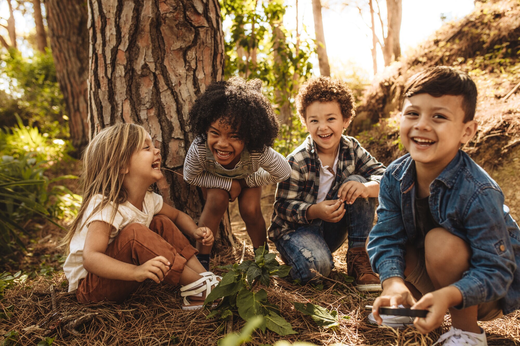 Vier fröhliche Kinder sitzen vor einem Baum im Grünen