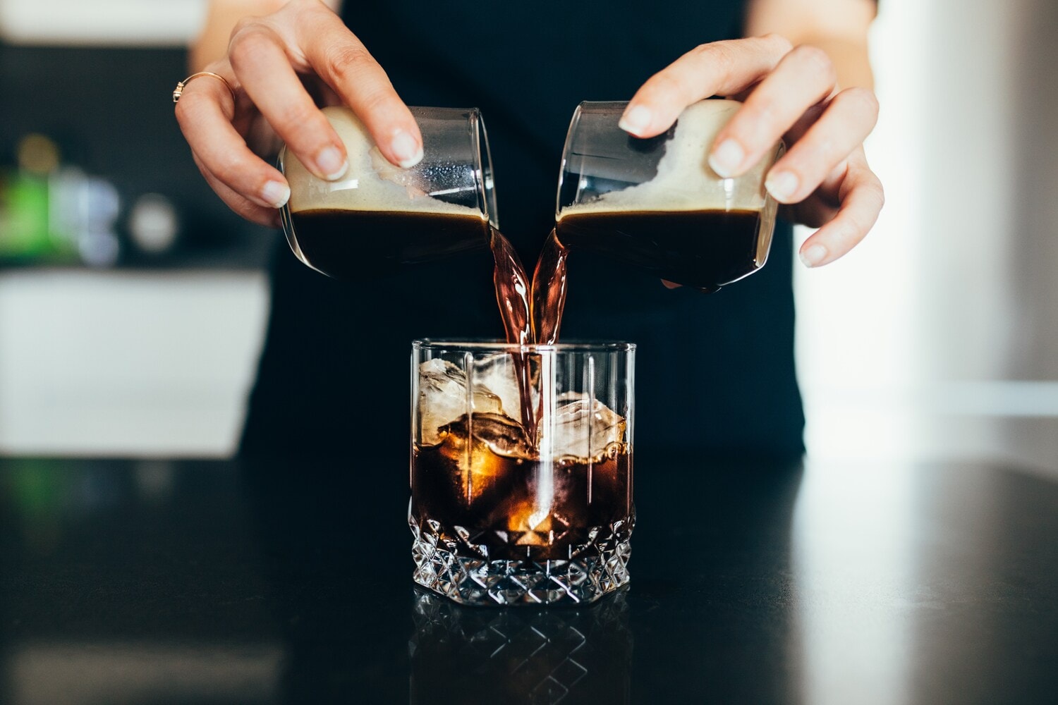 Eine Frau gießt kalten Kaffee in ein Glas mit Eiswürfeln