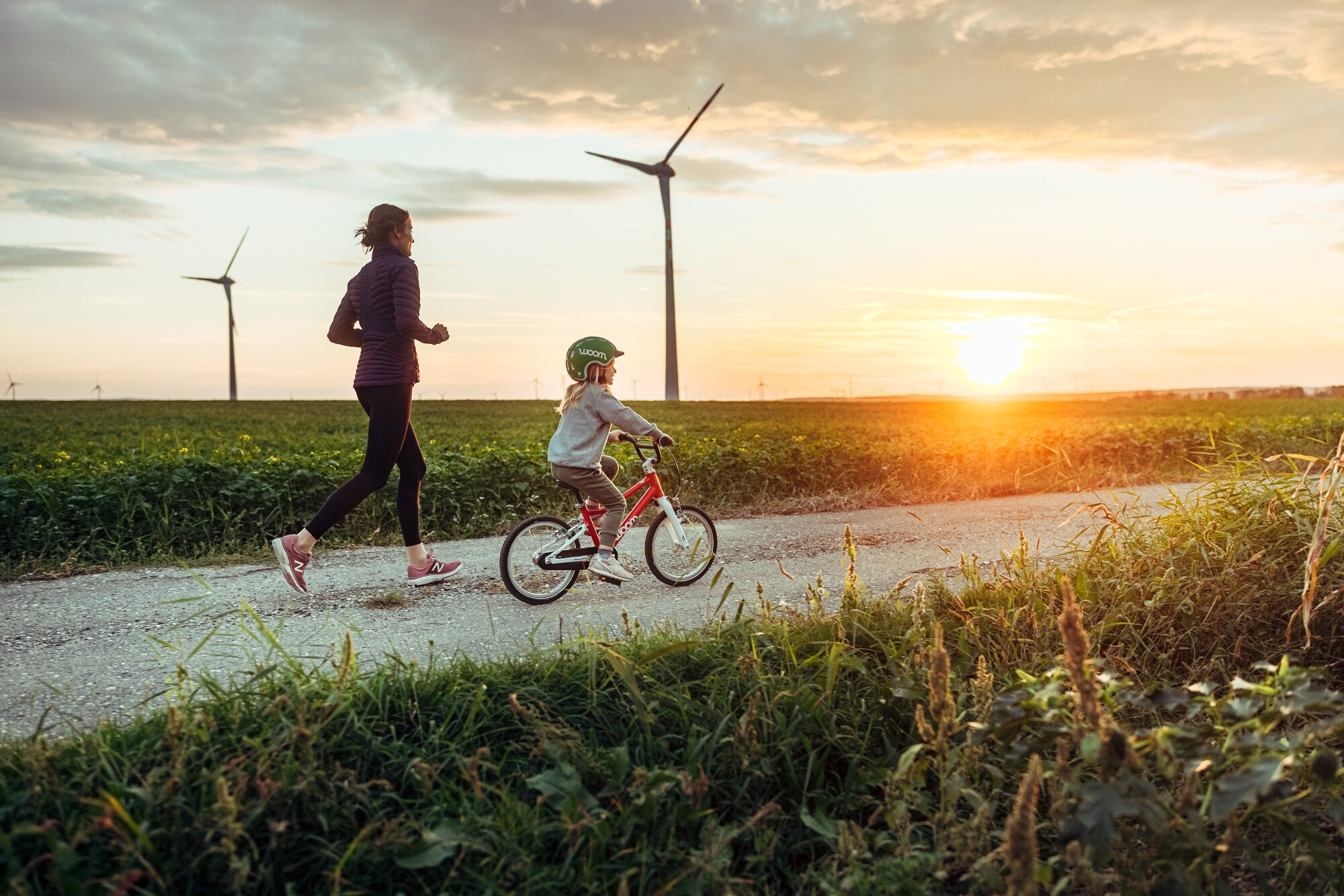 Eine joggende Frau ist mit einem kleinen Mädchen auf dem Fahrrad bei Sonnenuntergang unterwegs