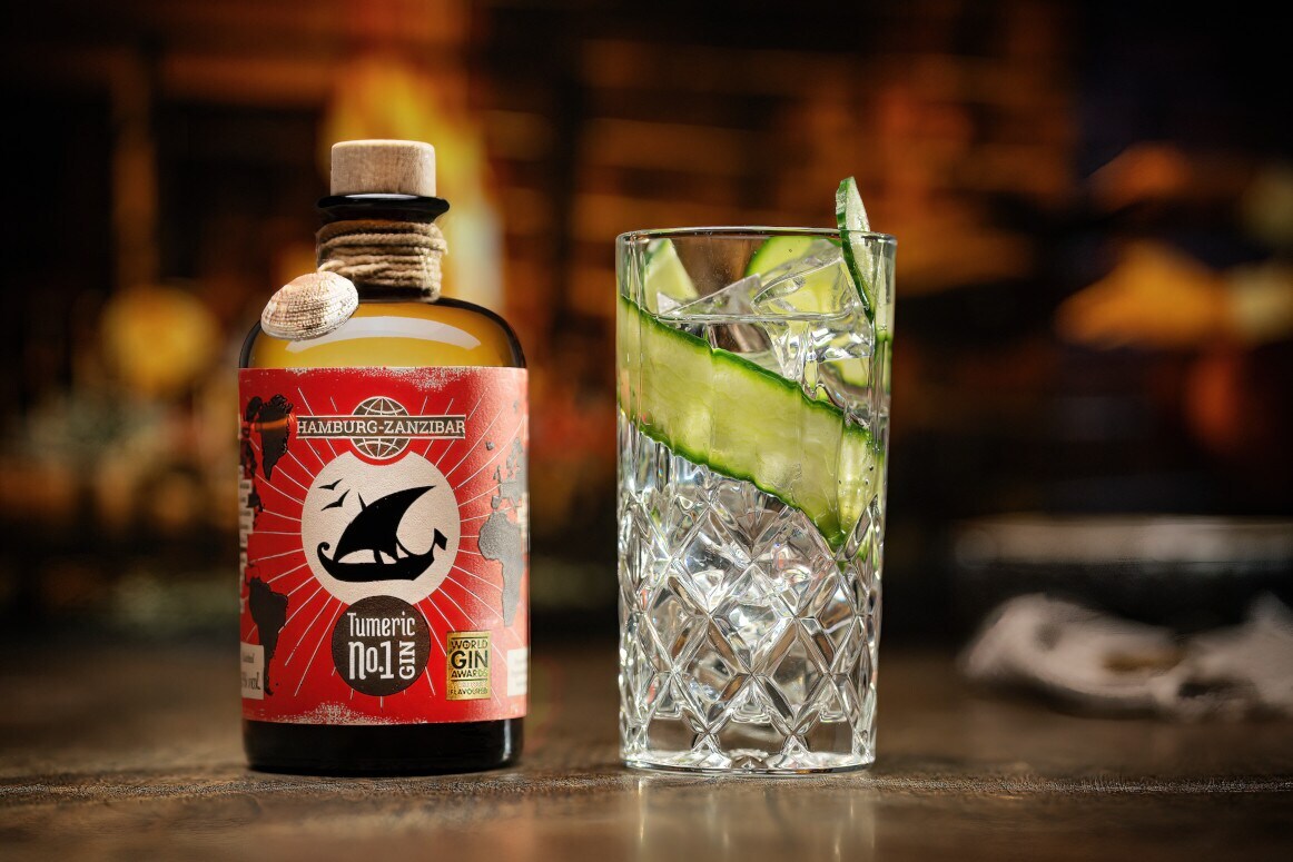 Flasche Gin neben einem Glas mit Eiswürfeln und Gurkenscheibe