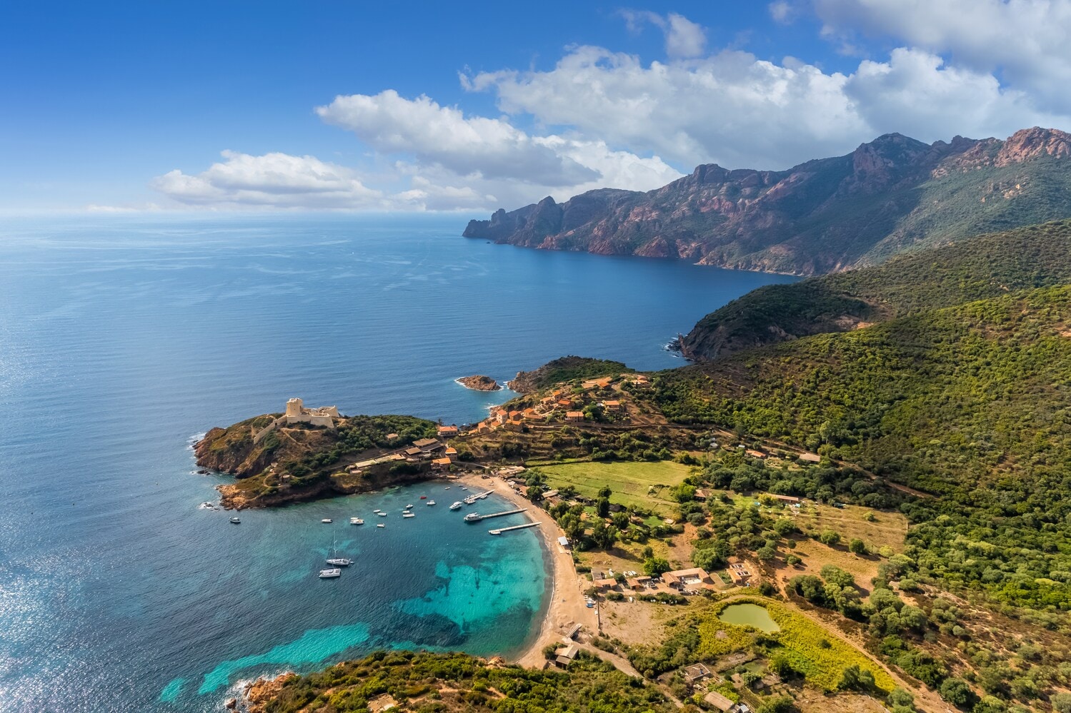 Blick über eine Bucht auf Korsika mit türkisem Wasser, ein paar Booten und einer Gebirgskette im Hintergrund. Blick über eine Bucht auf Korsika mit türkisem Wasser, ein paar Booten und einer Gebirgskette im Hintergrund.