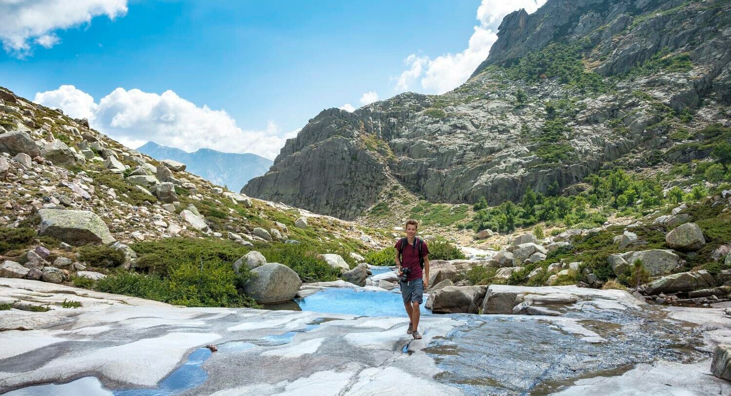 Ein Mann wandert über einen felsigen Untergrund mit blauem Himmel und Bergen im Hintergrund. Ein Mann wandert über einen felsigen Untergrund mit blauem Himmel und Bergen im Hintergrund.