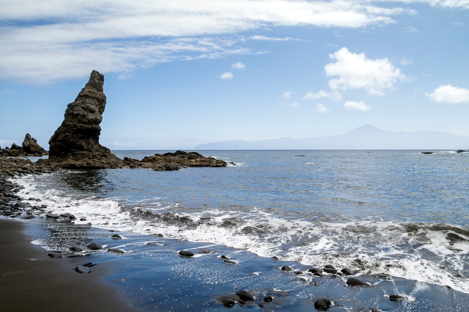 Sandstrand mit Steinen und Felsformationen, am Horizont ist der Teide auf Teneriffa zu erkennen. Sandstrand mit Steinen und Felsformationen, am Horizont ist der Teide auf Teneriffa zu erkennen.