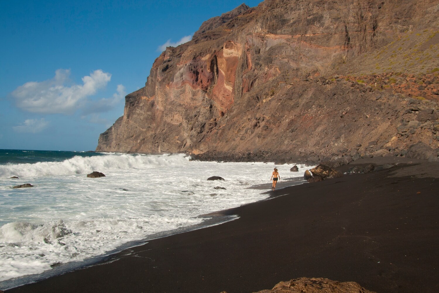 Dunkler Sandstrand, hohe Felsen und mäßiger Wellengang. Dunkler Sandstrand, hohe Felsen und mäßiger Wellengang.