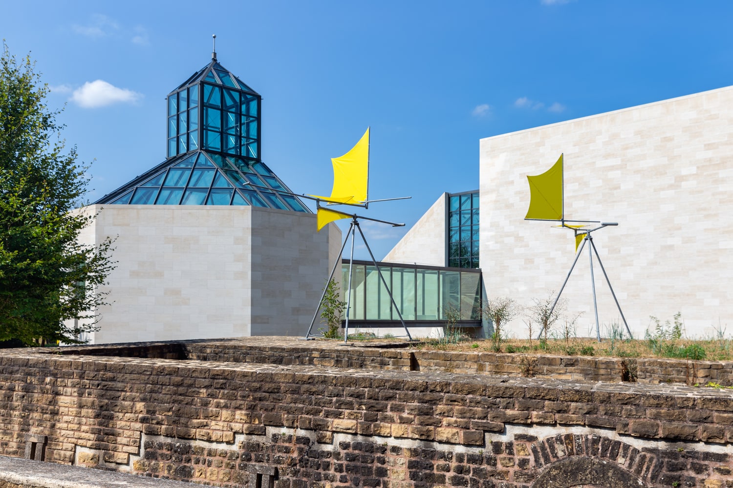 Ein modernes Gebäude vor dem eine gelbe Kunst-Installation steht. Ein modernes Gebäude vor dem eine gelbe Kunst-Installation steht.