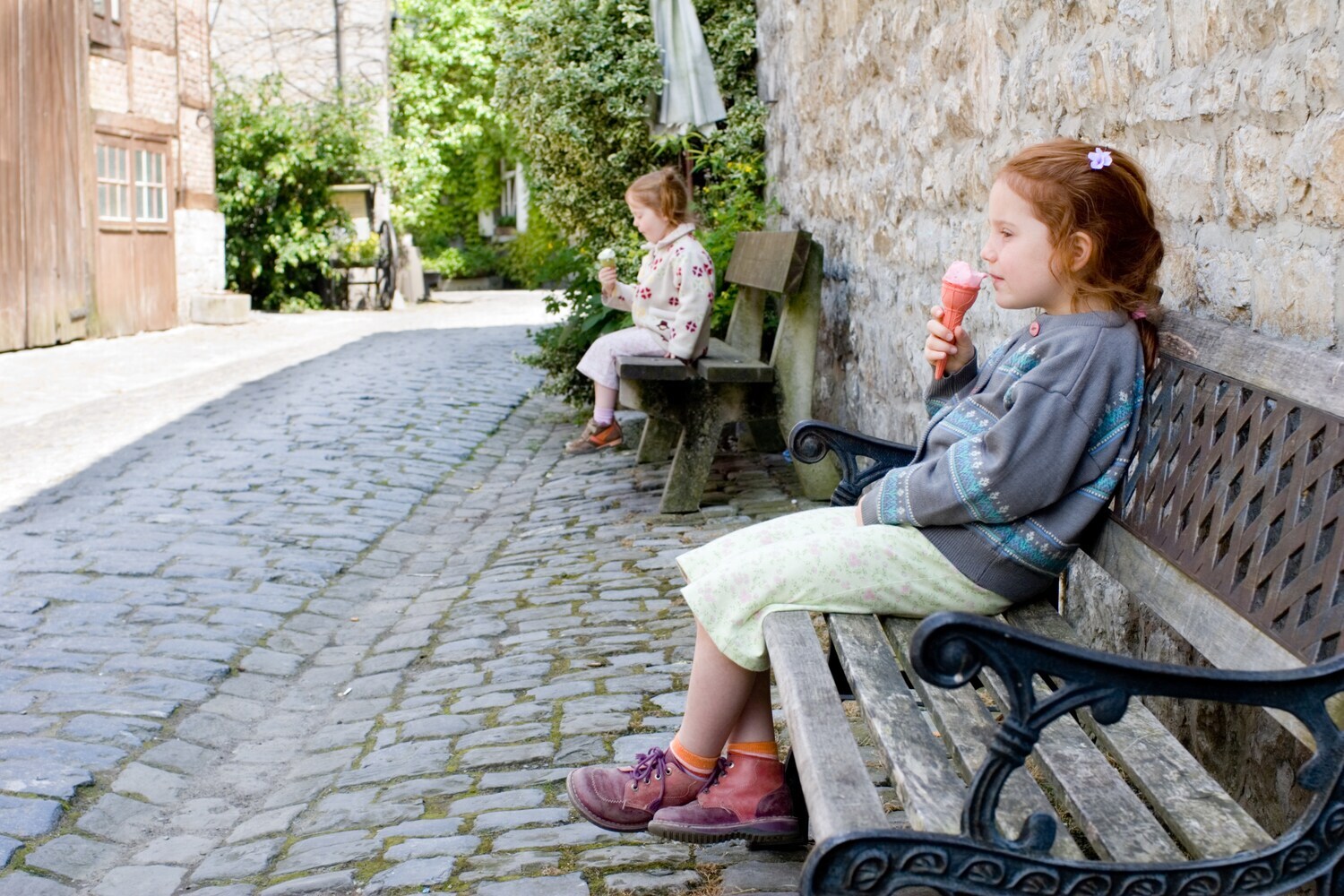 Zwei Mädchen sitzen in einer historischen Gasse jeweils auf einer Bank.