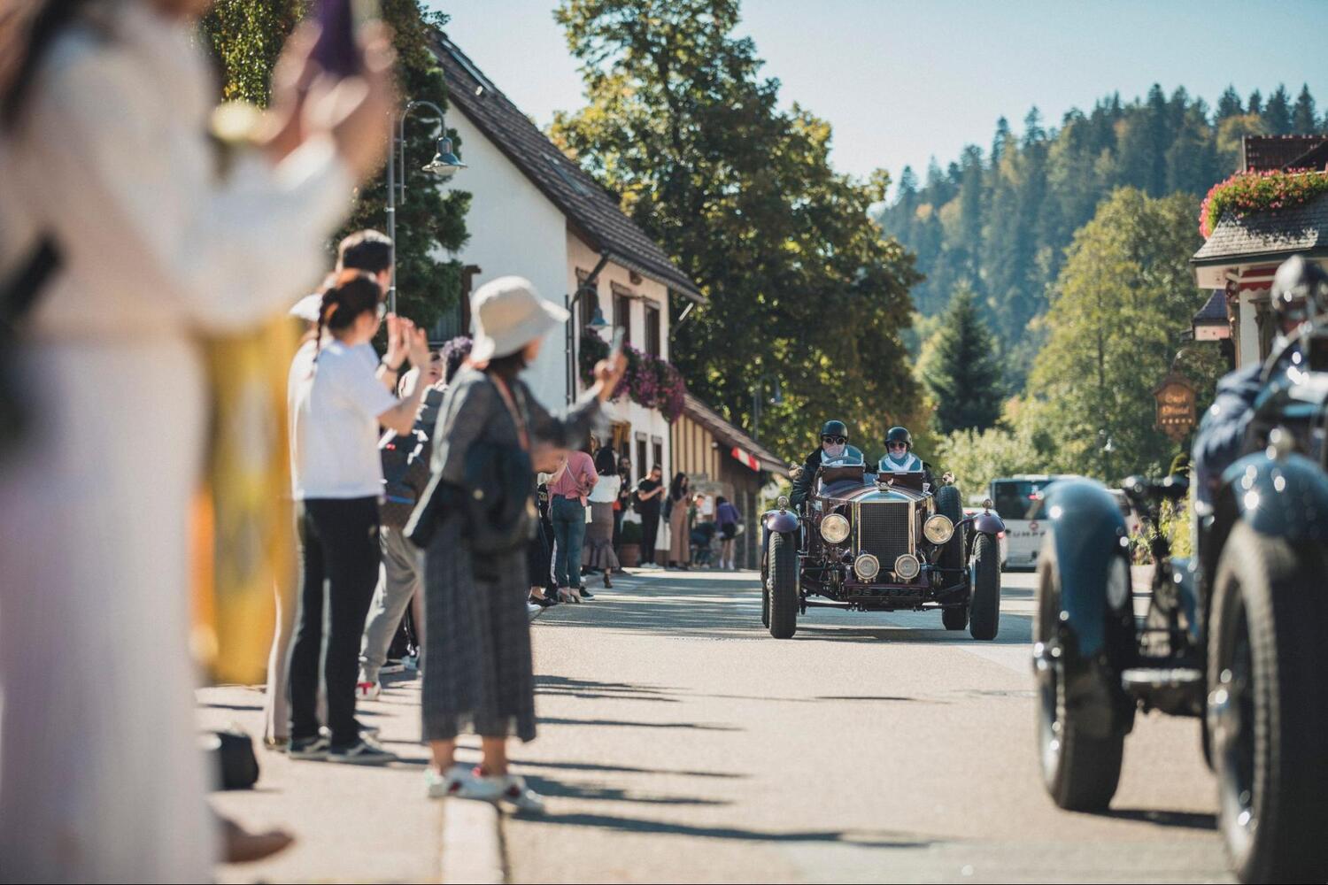 Zuschauer beklatschen Oldtimer auf einer Straße Zuschauer beklatschen Oldtimer auf einer Straße