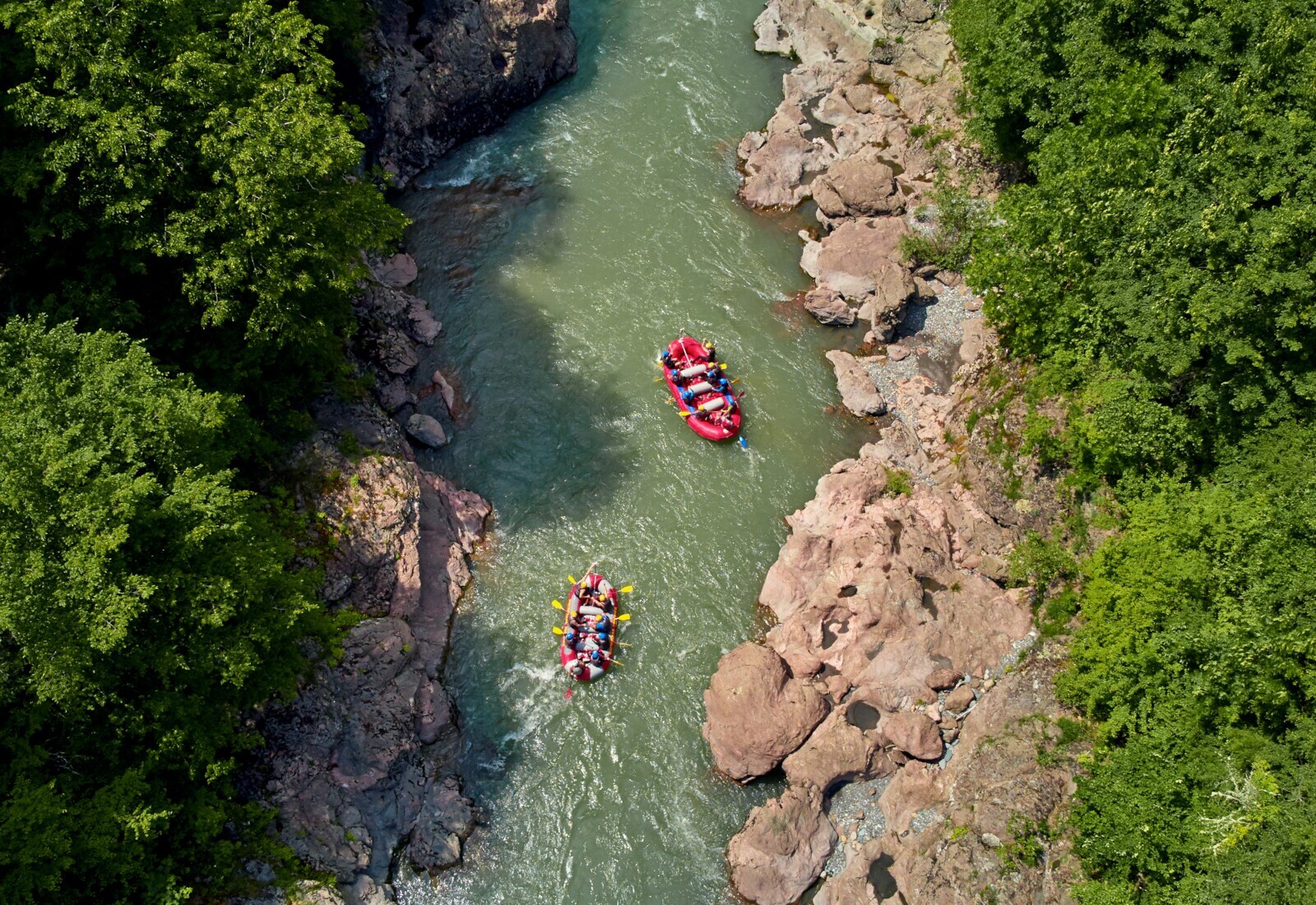 Luftaufnahme zweier Raftingboote in einem Fluss zwischen Felsen und Bäumen Luftaufnahme zweier Raftingboote in einem Fluss zwischen Felsen und Bäumen