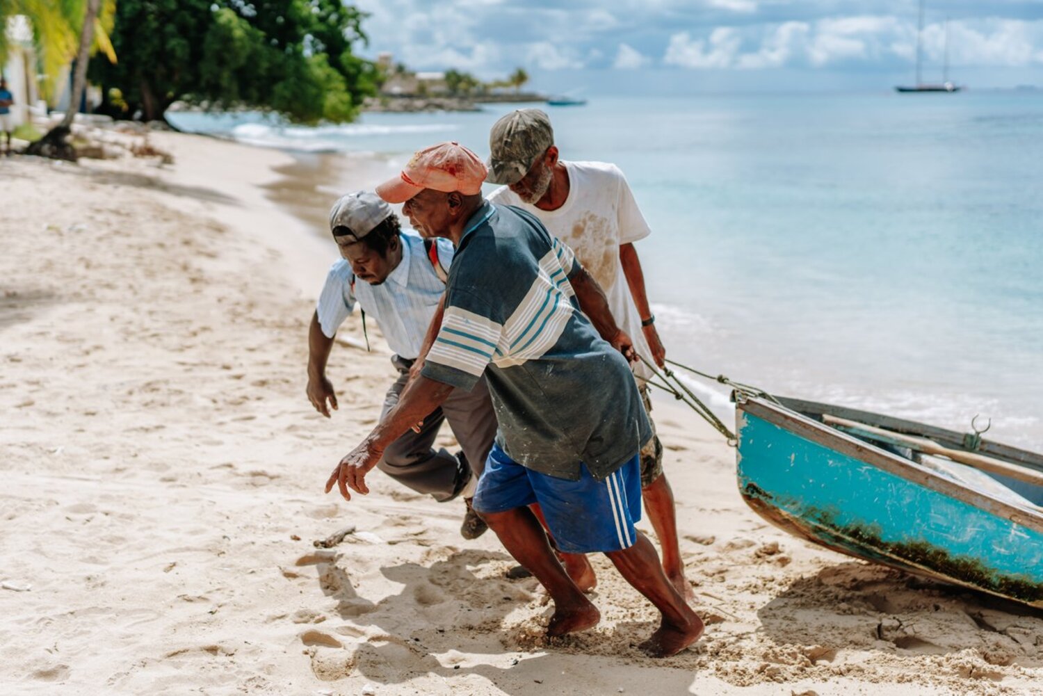 Drei Männer ziehen per Hand ein kleines Boot an den Strand.