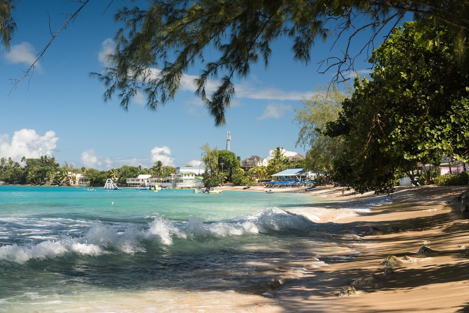 Ein Strandabschnitt mit türkisblauem Wasser und Bäumen, im Hintergrund einige Beach-Häuser.