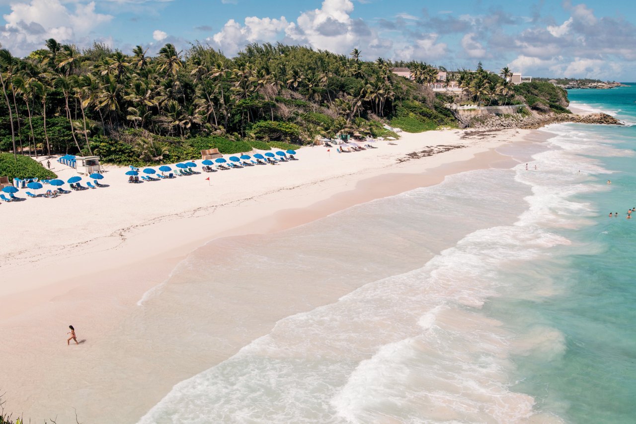 Sonnenliegen am weißen Sandstrand mit türkisblauem Wasser, ein Hotel im Hintergrund.