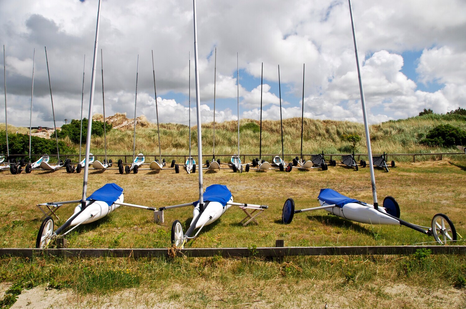 Mehrere Strandsegler parken vor einer Düne.
