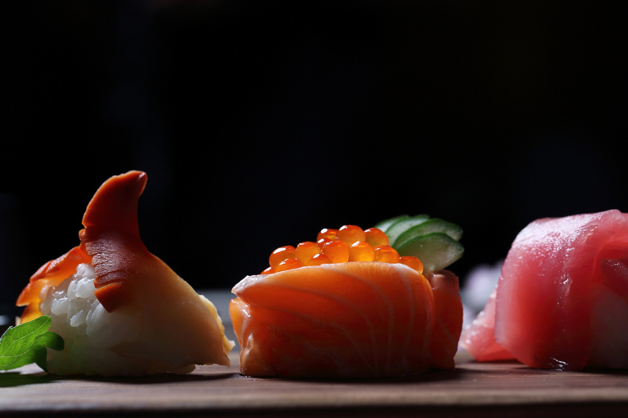 Drei verschiedene Sushi vor einem schwarzen Hintergrund.