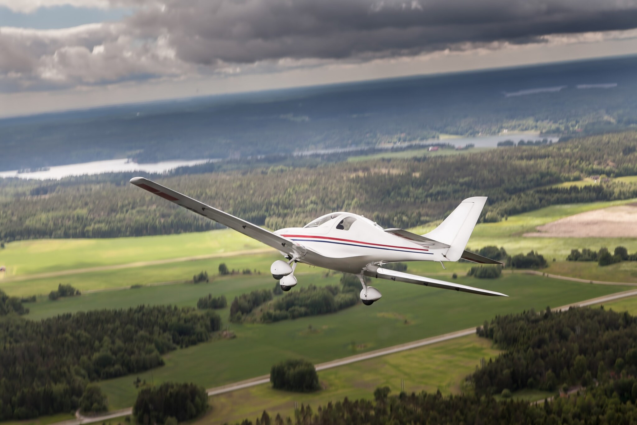 Ein Ultraleichtflugzeug, das über eine flache Landschaft mit Wäldern, Feldern und Fluss fliegt