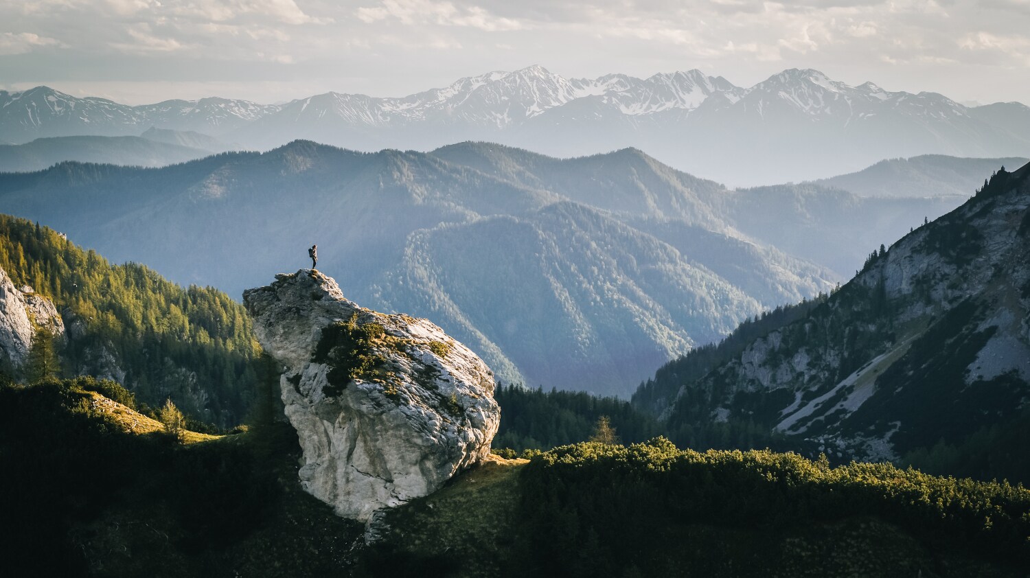 Eine Person beim Wandern auf einem Felsen umgeben von Bergen Eine Person beim Wandern auf einem Felsen umgeben von Bergen