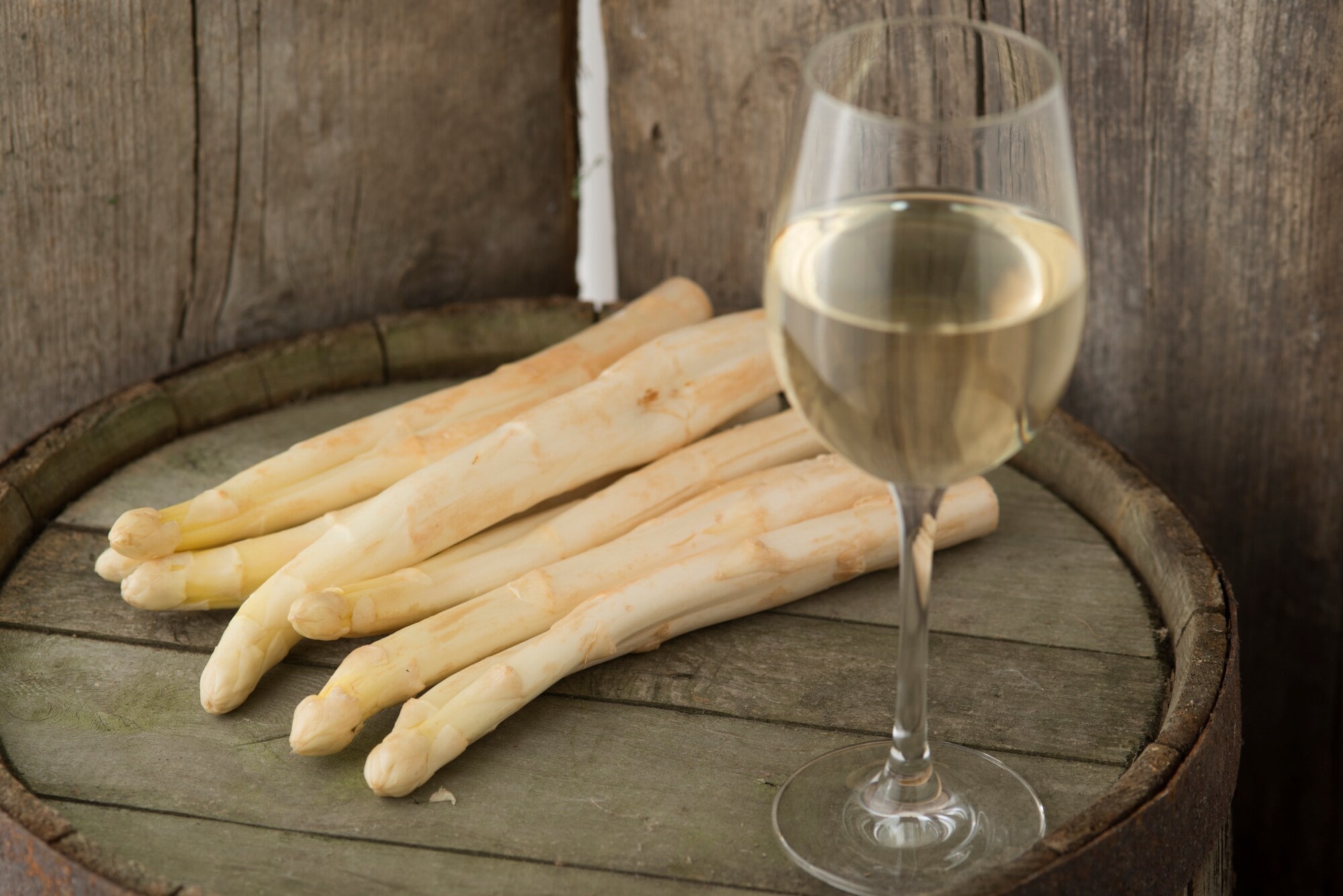 Ein Glas Wein und mehrere Stangen Spargel auf einem Fass Wein
