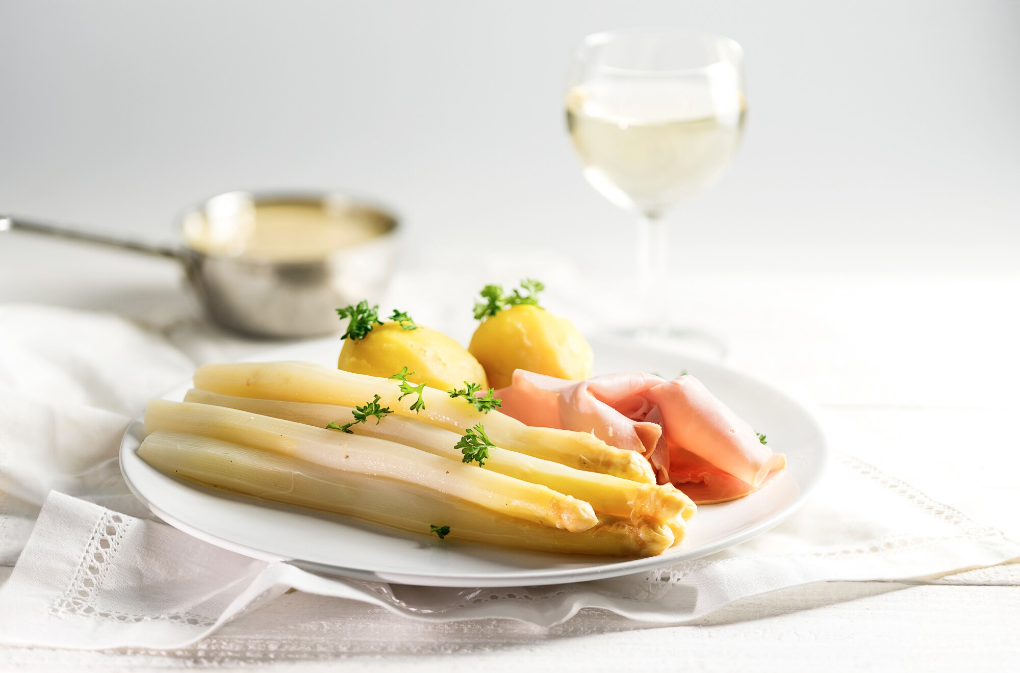 Ein Teller mit Spargel, Kartoffeln und Schinken mit einem Glas Wein