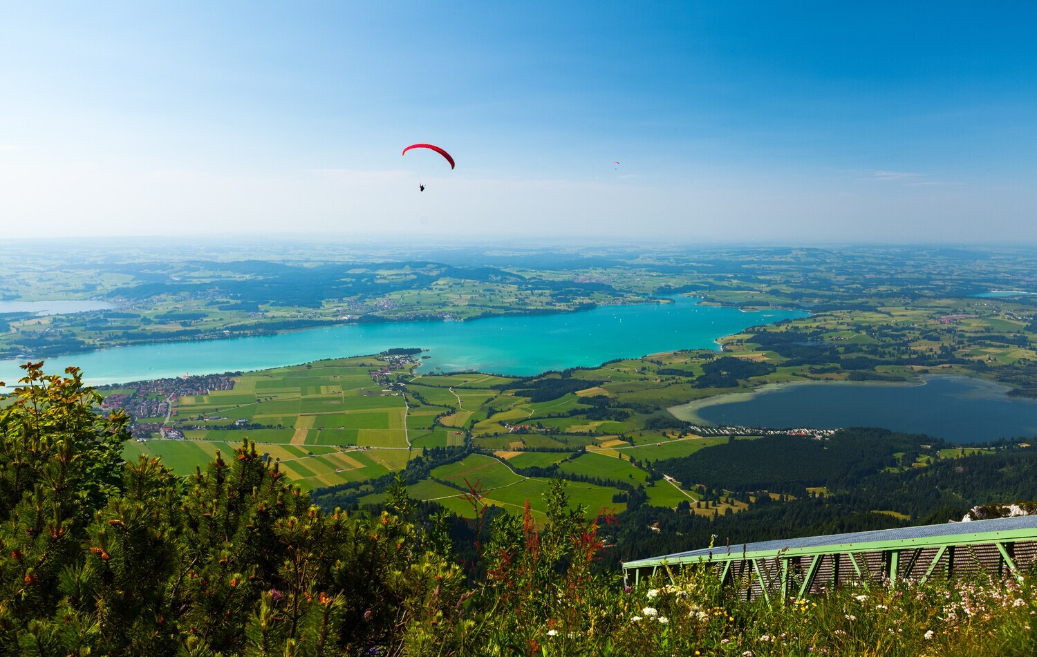 Ein Paraglider fliegt über eine Landschaft, bestehend aus Feldern und Seen.