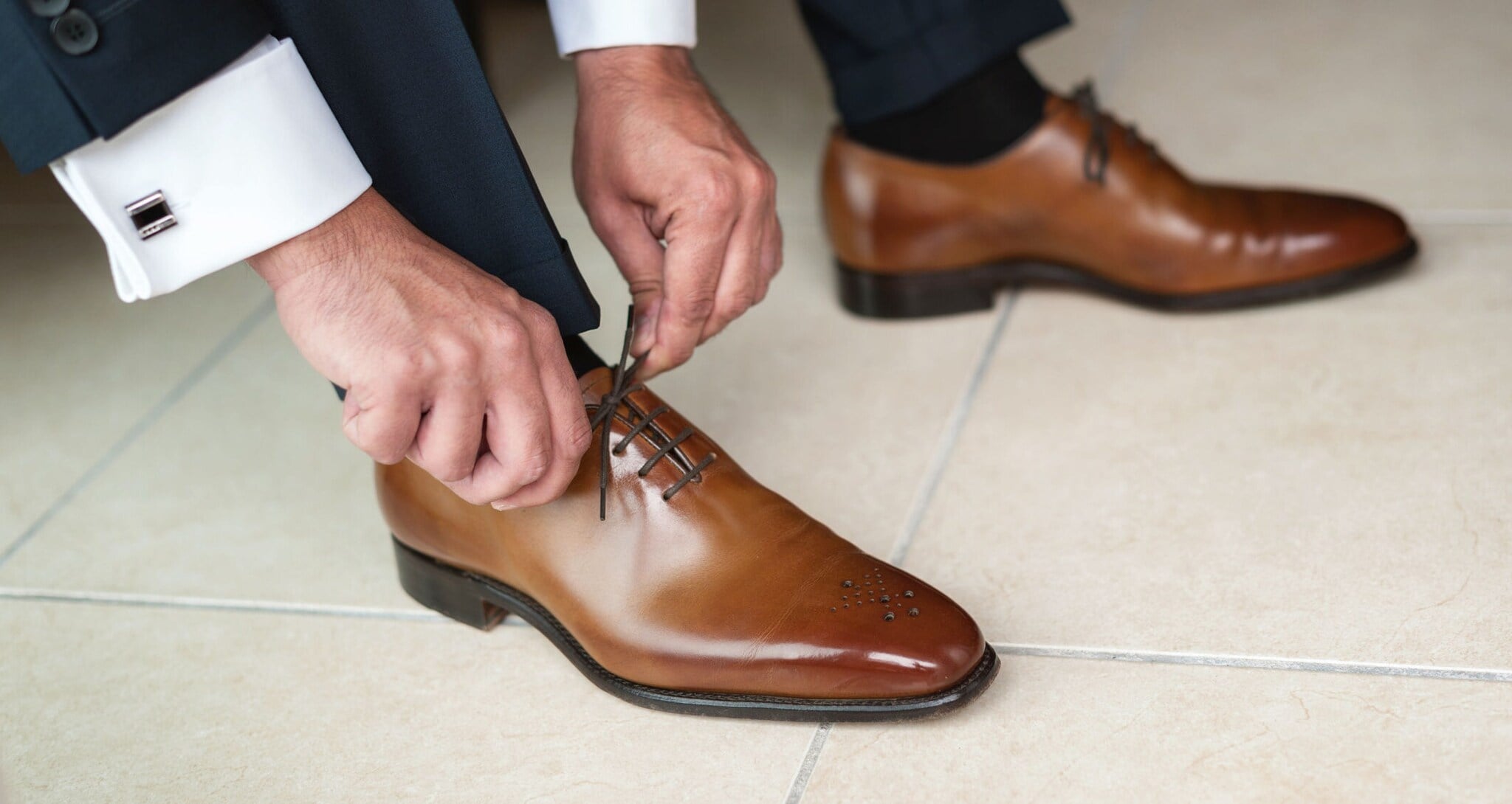 Nahaufnahme von schicken, braunen Lederschuhen, die von einem Herren im Anzug zugeschnürt werden Nahaufnahme von schicken, braunen Lederschuhen, die von einem Herren im Anzug zugeschnürt werden