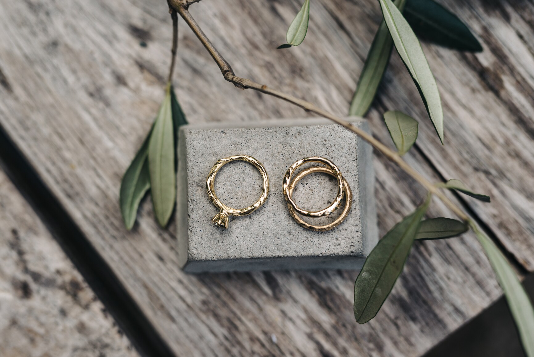 Drei handgefertigte Trauringe aus Gold auf einem Betonblock