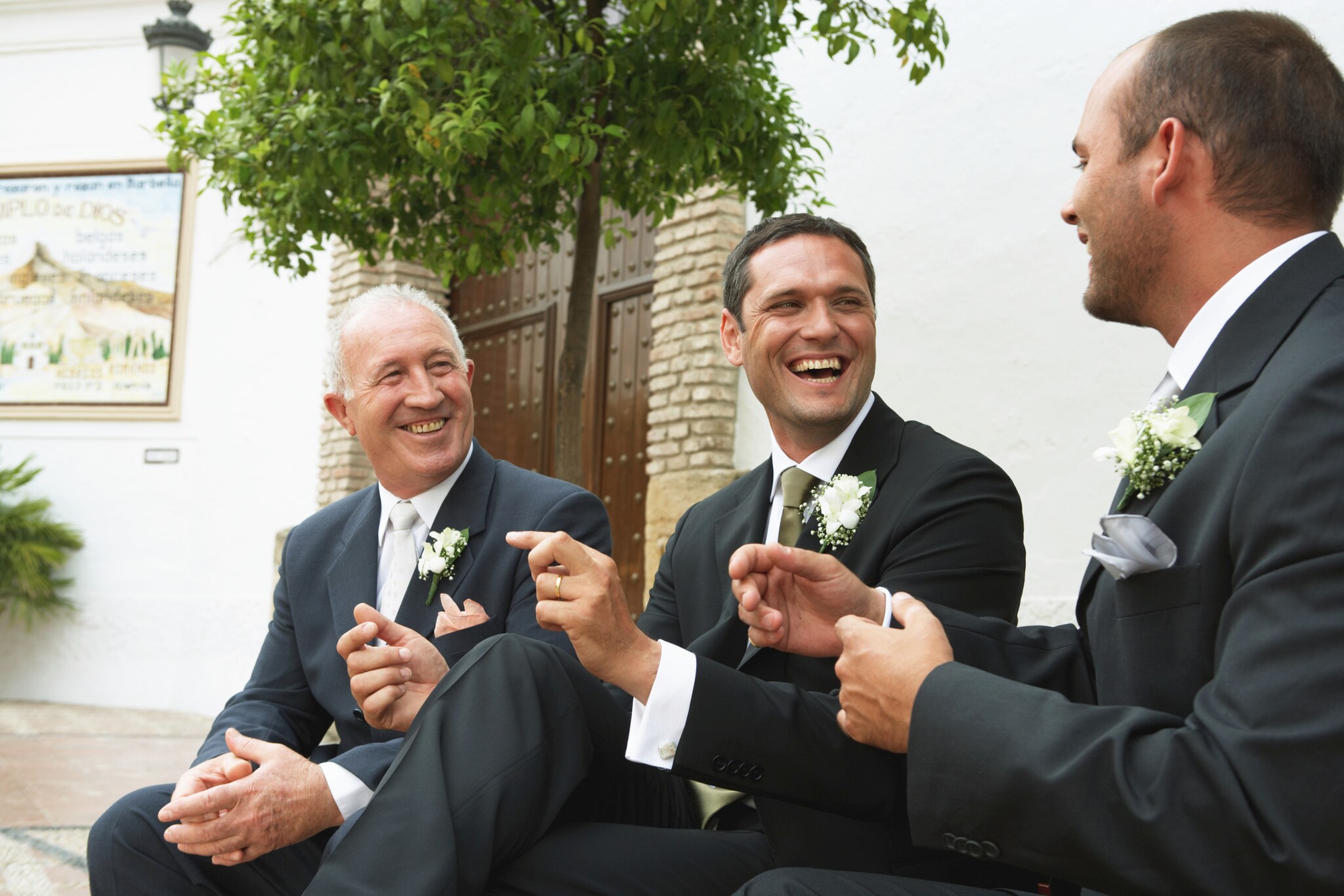 Drei lachende Männer in Anzügen sitzen vor einer Kirche