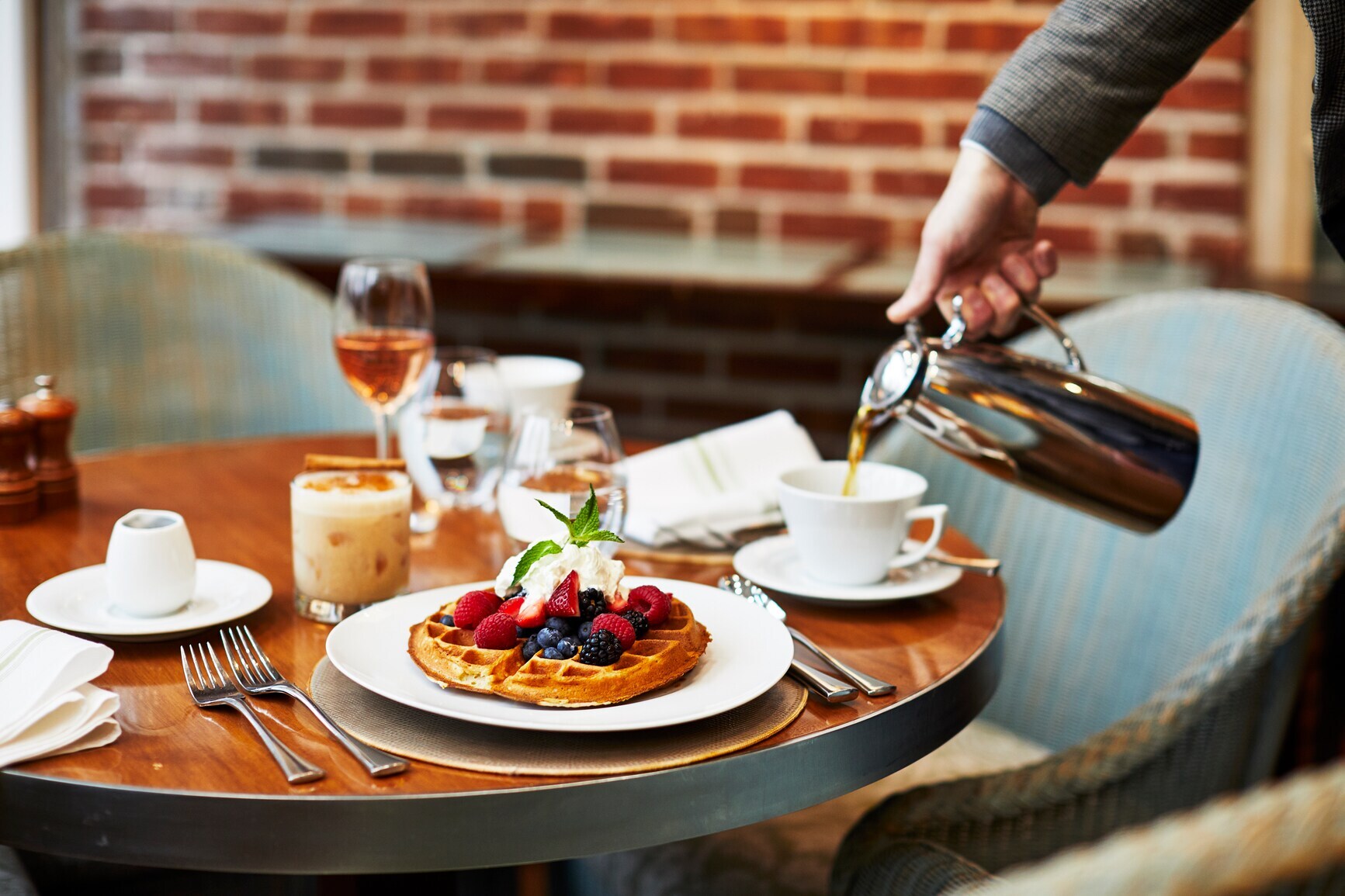 Eine Tasse Kaffee wird neben einem Teller mit Waffeln auf einem gedeckten Frühstückstisch eingegossen