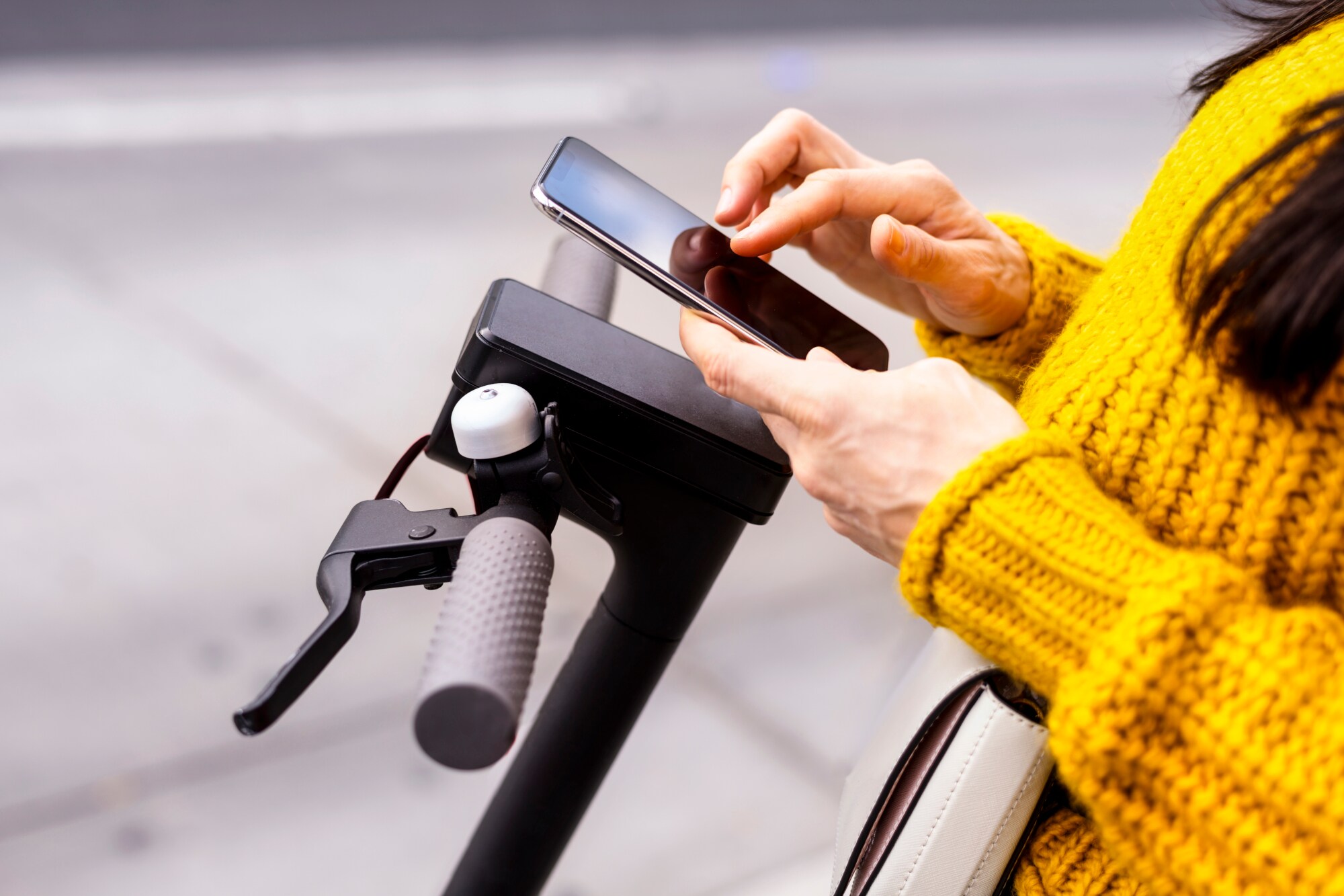Nahaufnahme von zwei Händen, die ein Smartphone vor einem E-Scooter bedienen Nahaufnahme von zwei Händen, die ein Smartphone vor einem E-Scooter bedienen