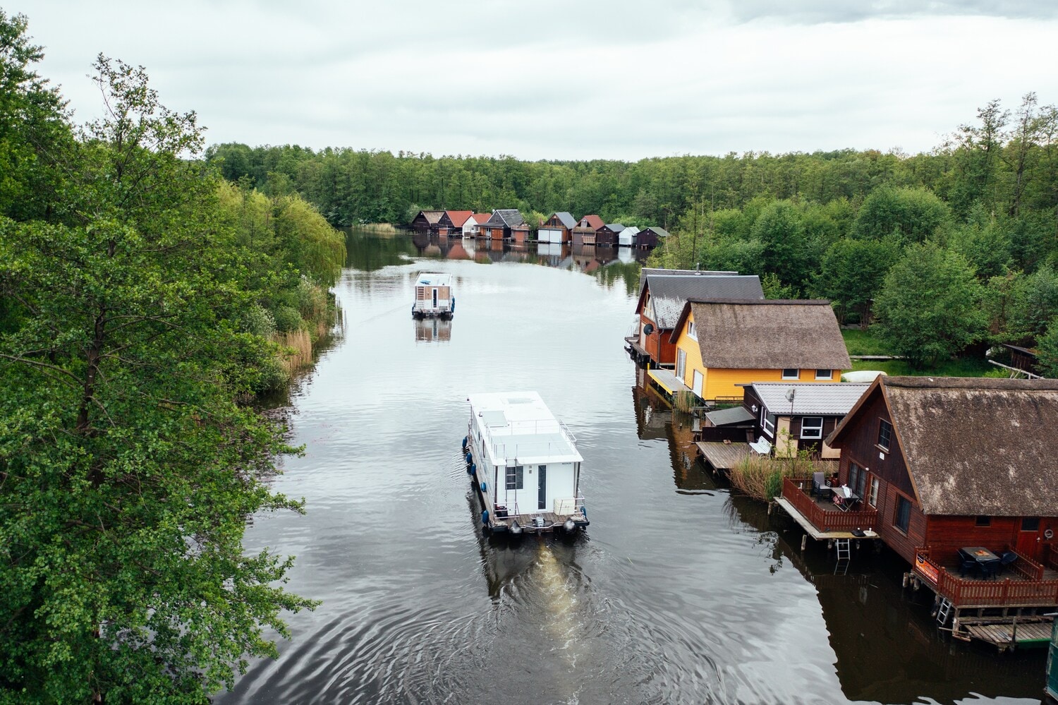 Hausboote schippern übers Wasser, am Rand stehen kleine Hütten Hausboote schippern übers Wasser, am Rand stehen kleine Hütten