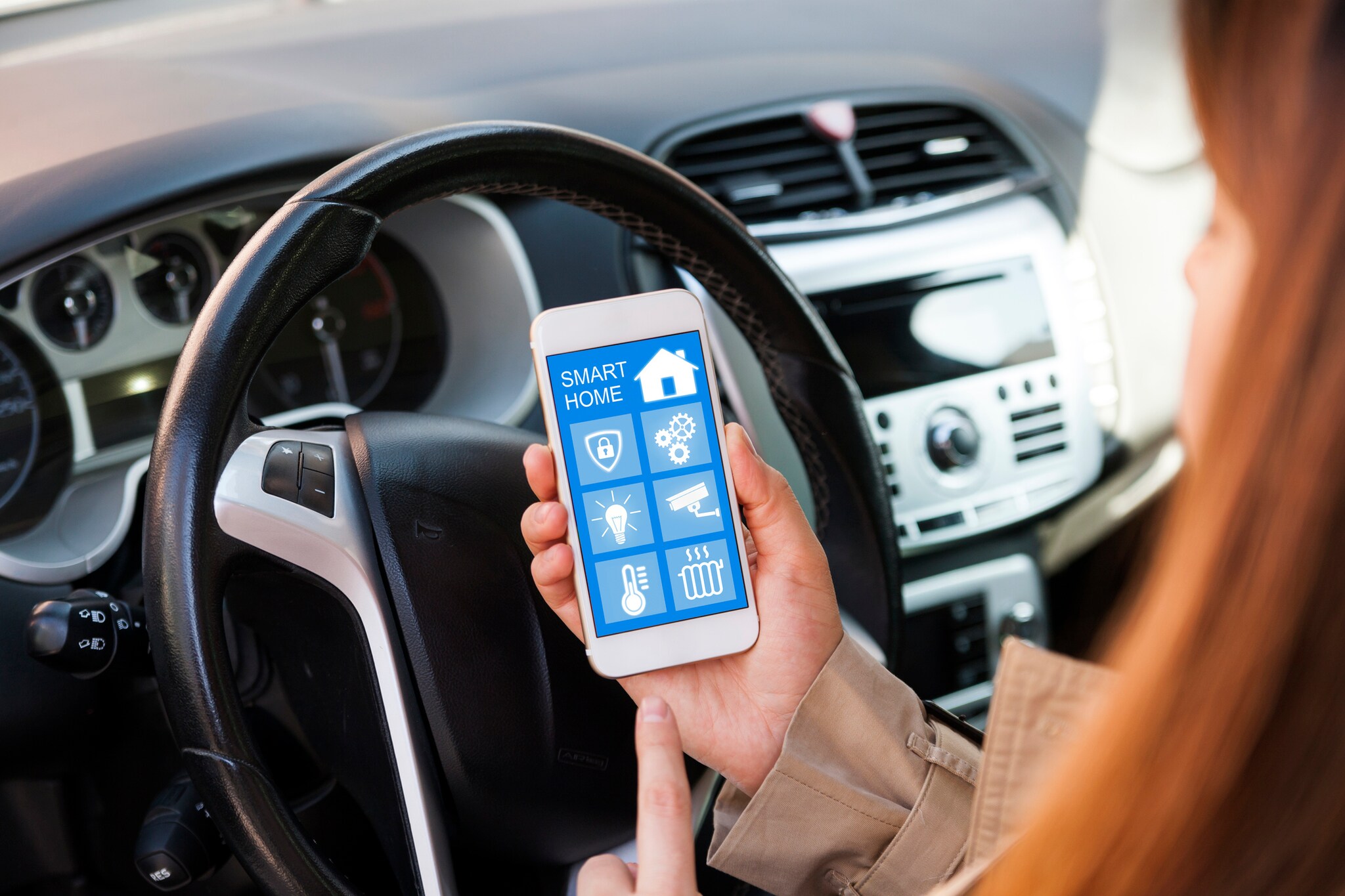 Frau im Auto blick auf ihr Handy und kontrolliert ihr Smarthome