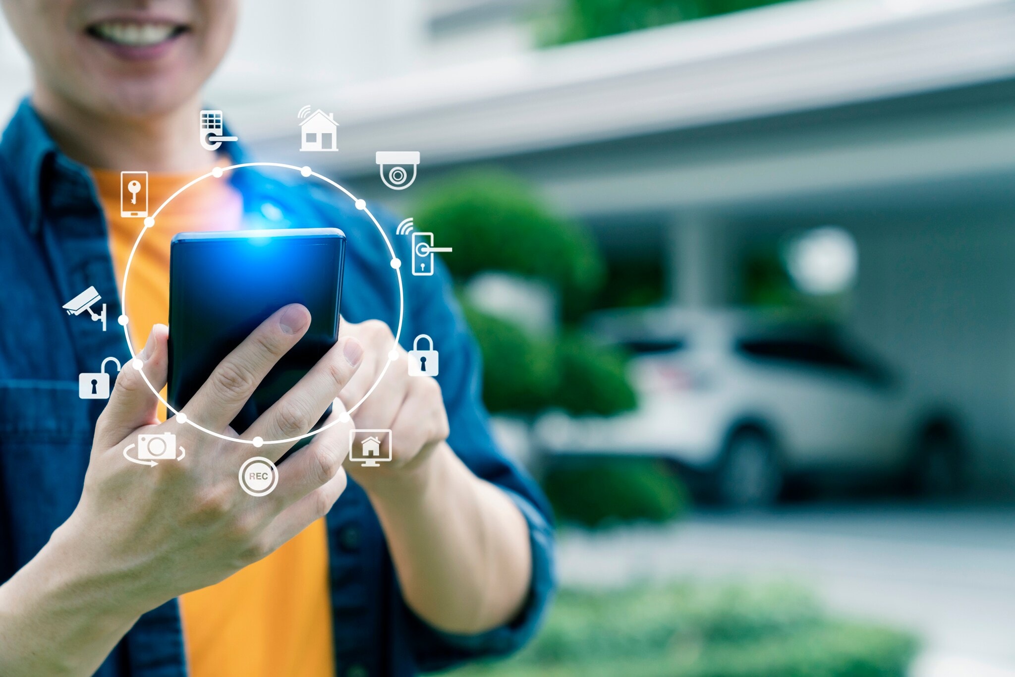 Person mit Smartphone, im Hintergrund ein Auto vor einer Garage Person mit Smartphone, im Hintergrund ein Auto vor einer Garage